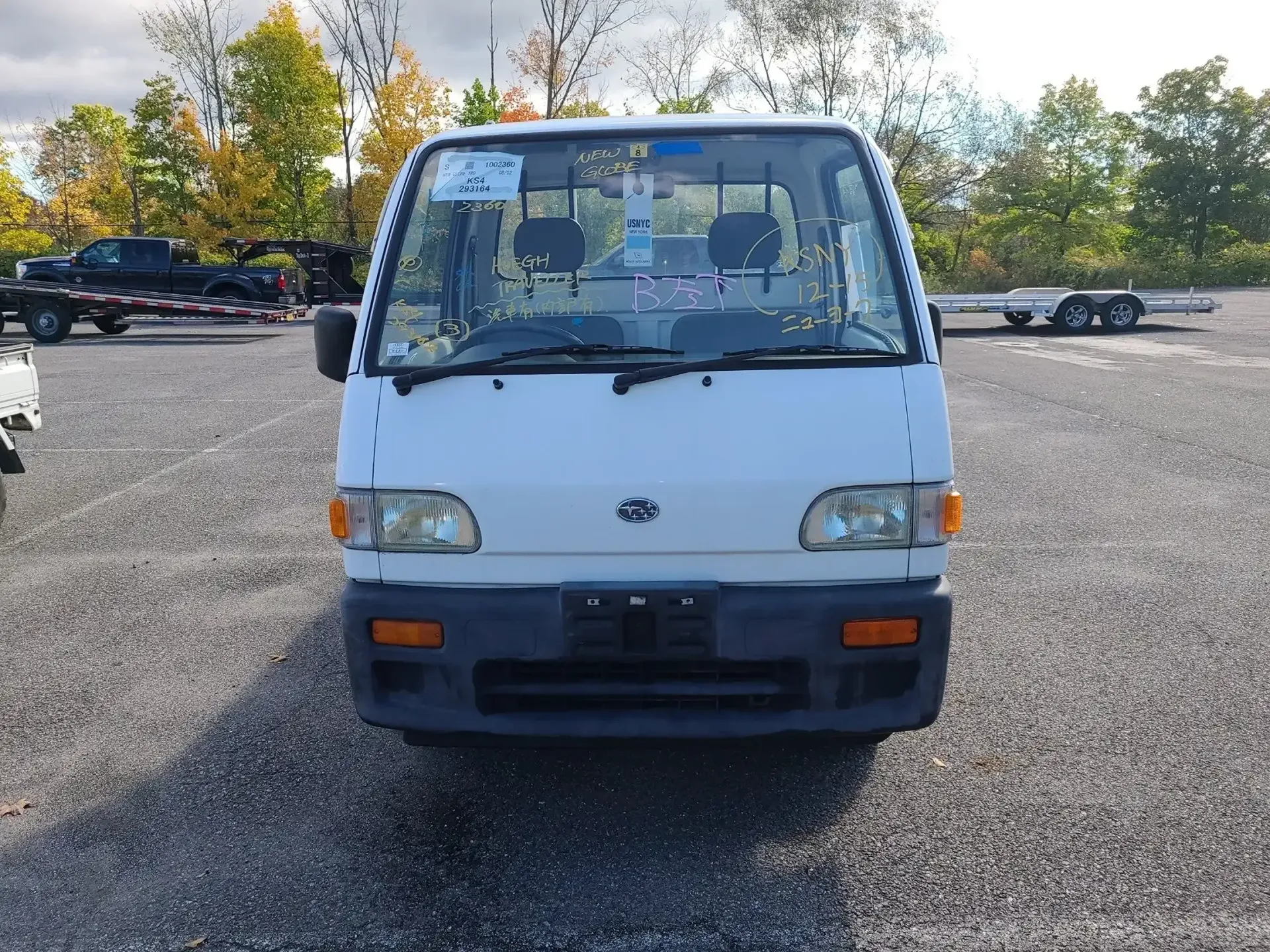 A white kei truck parked on a gravel lot under a cloudy sky.