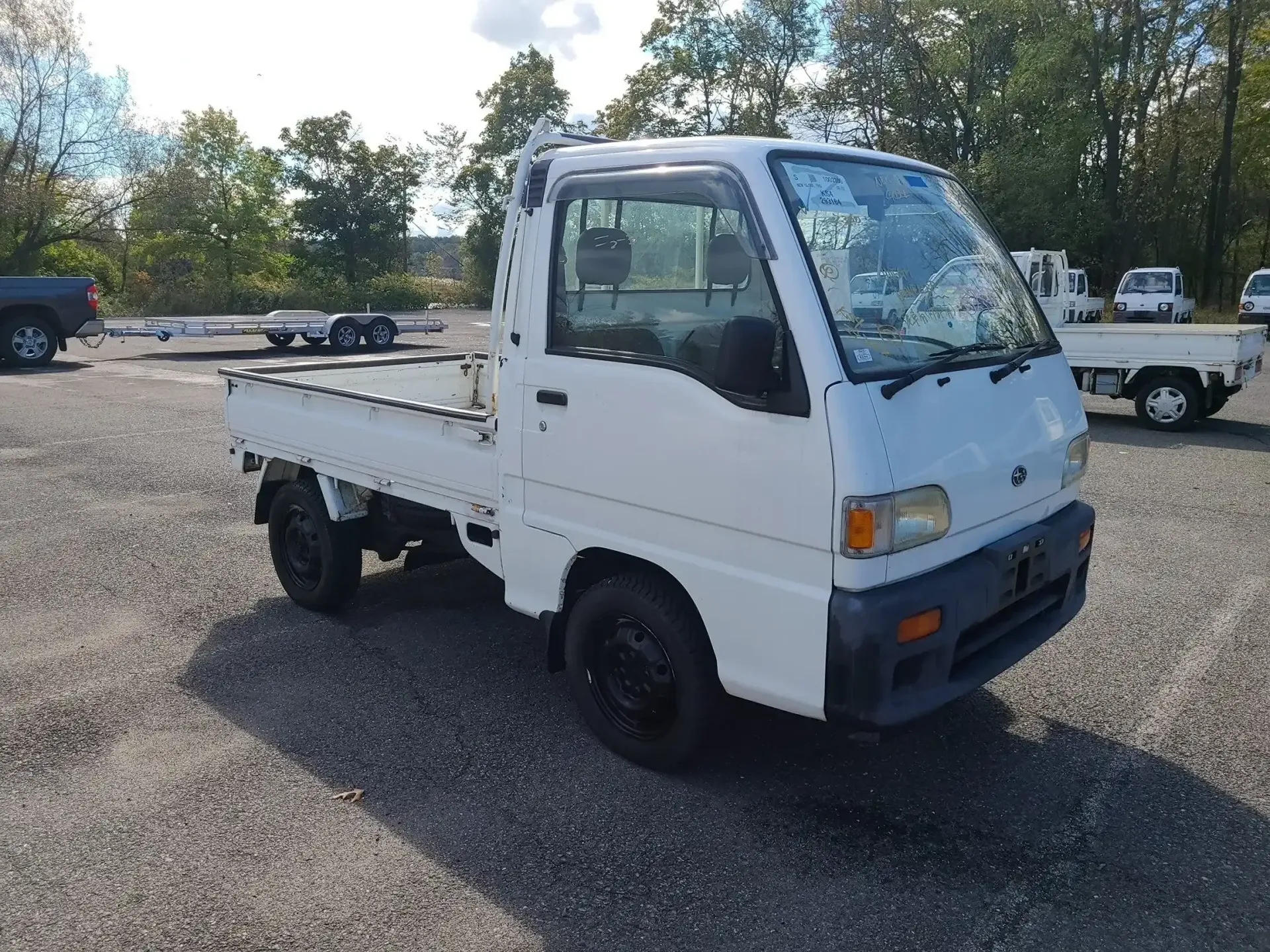 A white, compact Mitsubishi kei truck parked on a gravel lot under a bright, sunny sky.