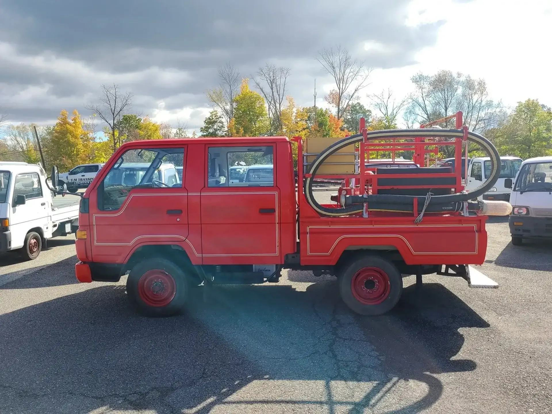 A red double-cab utility truck with an attached drilling or specialized rig on the flatbed, parked in a gravel lot.