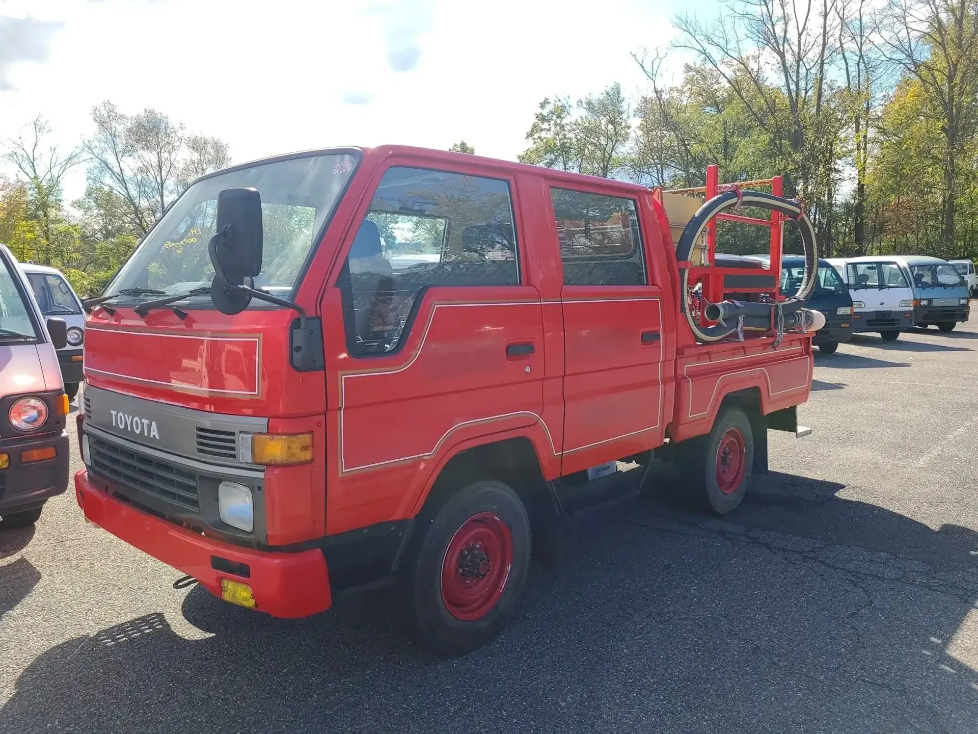 A red, four-door Toyota Dyna utility truck parked on a gravel lot with a piece of machinery mounted in the truck bed.