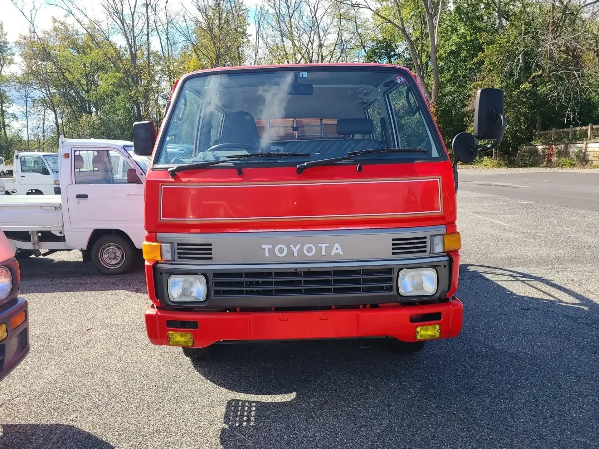 A red Toyota truck parked on a gravel lot, with a smaller white truck visible in the background.
