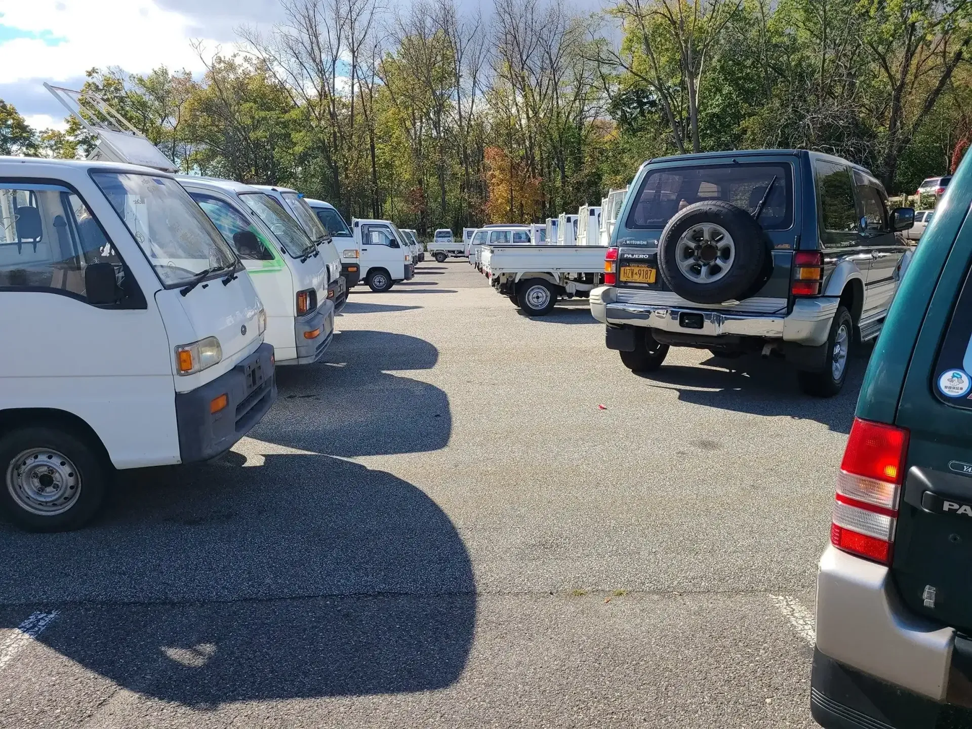 A gravel lot filled with various parked vehicles, including several white microvans and a dark SUV, under a cloudy sky.