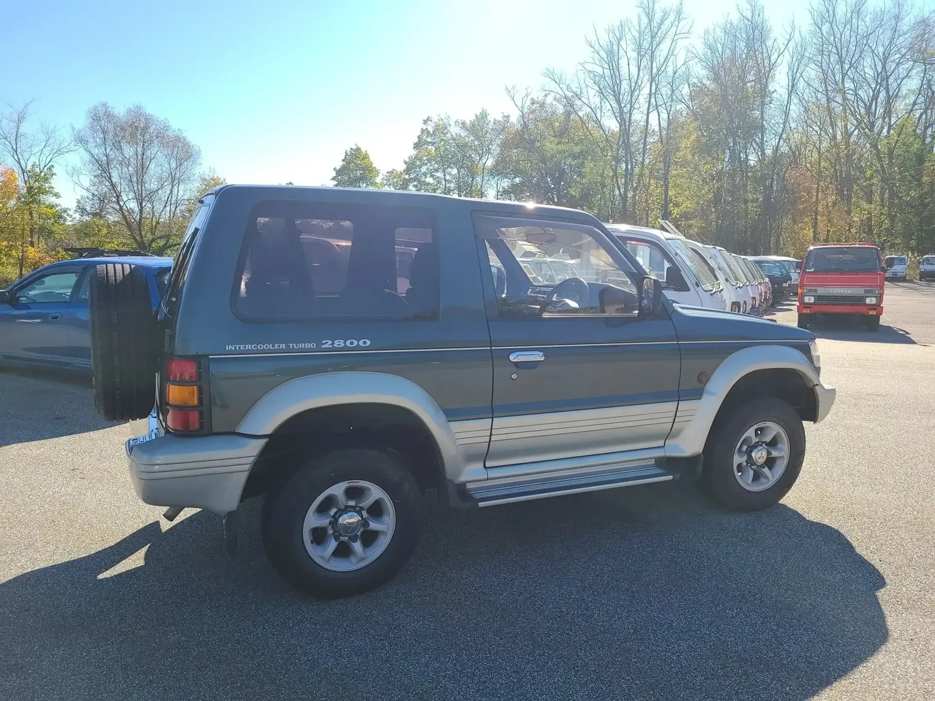 A dark green two-door SUV with silver accents parked on a gravel lot under a clear blue sky.