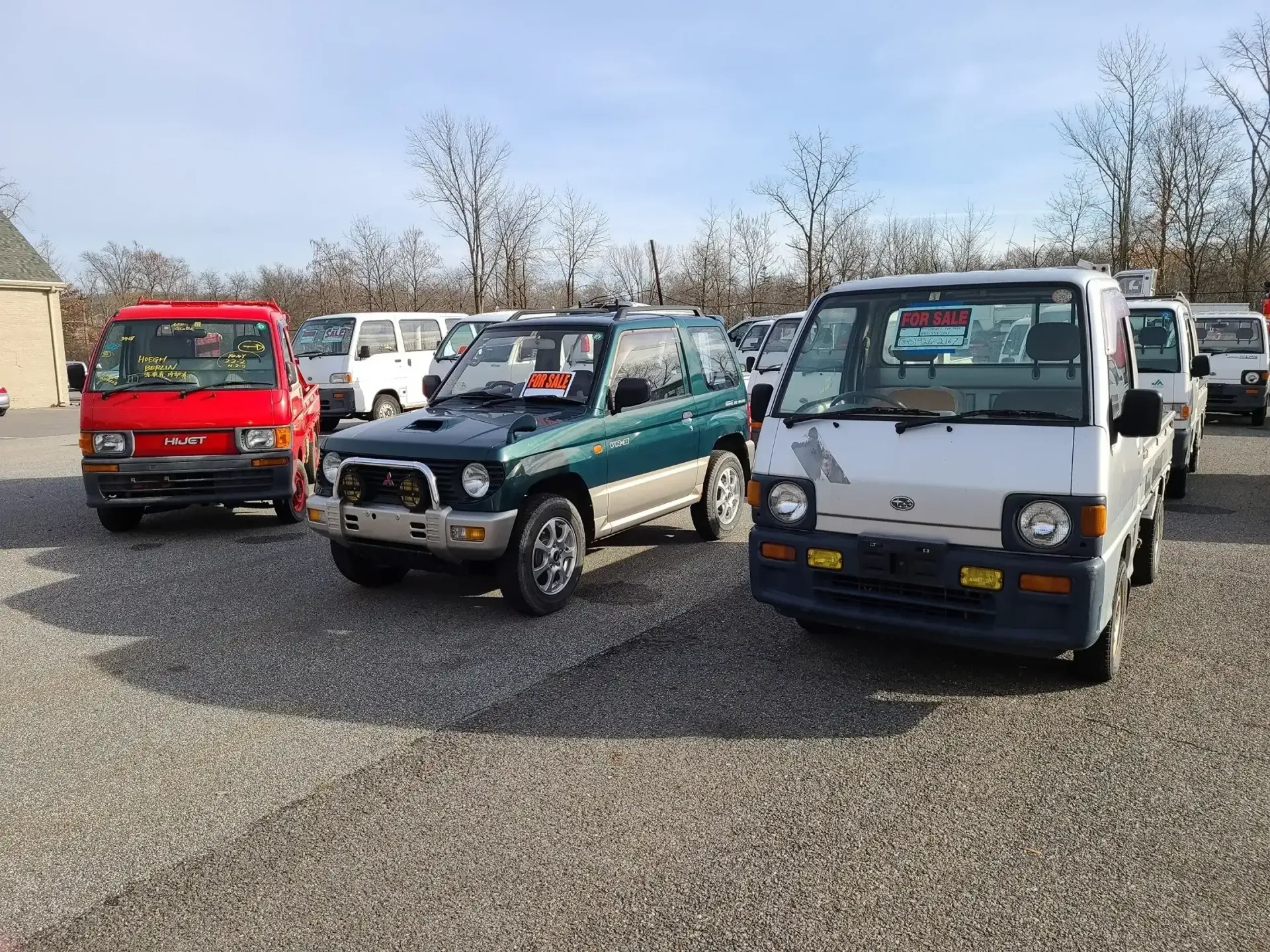 A parking lot with a red van, a green SUV, and a silver truck parked on a gravel surface under a clear blue sky.