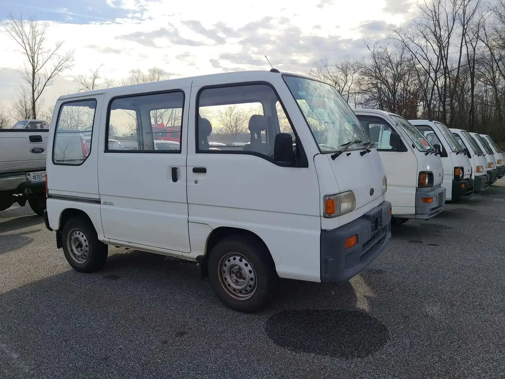 A row of white compact vans parked on a gravel lot during a sunset.