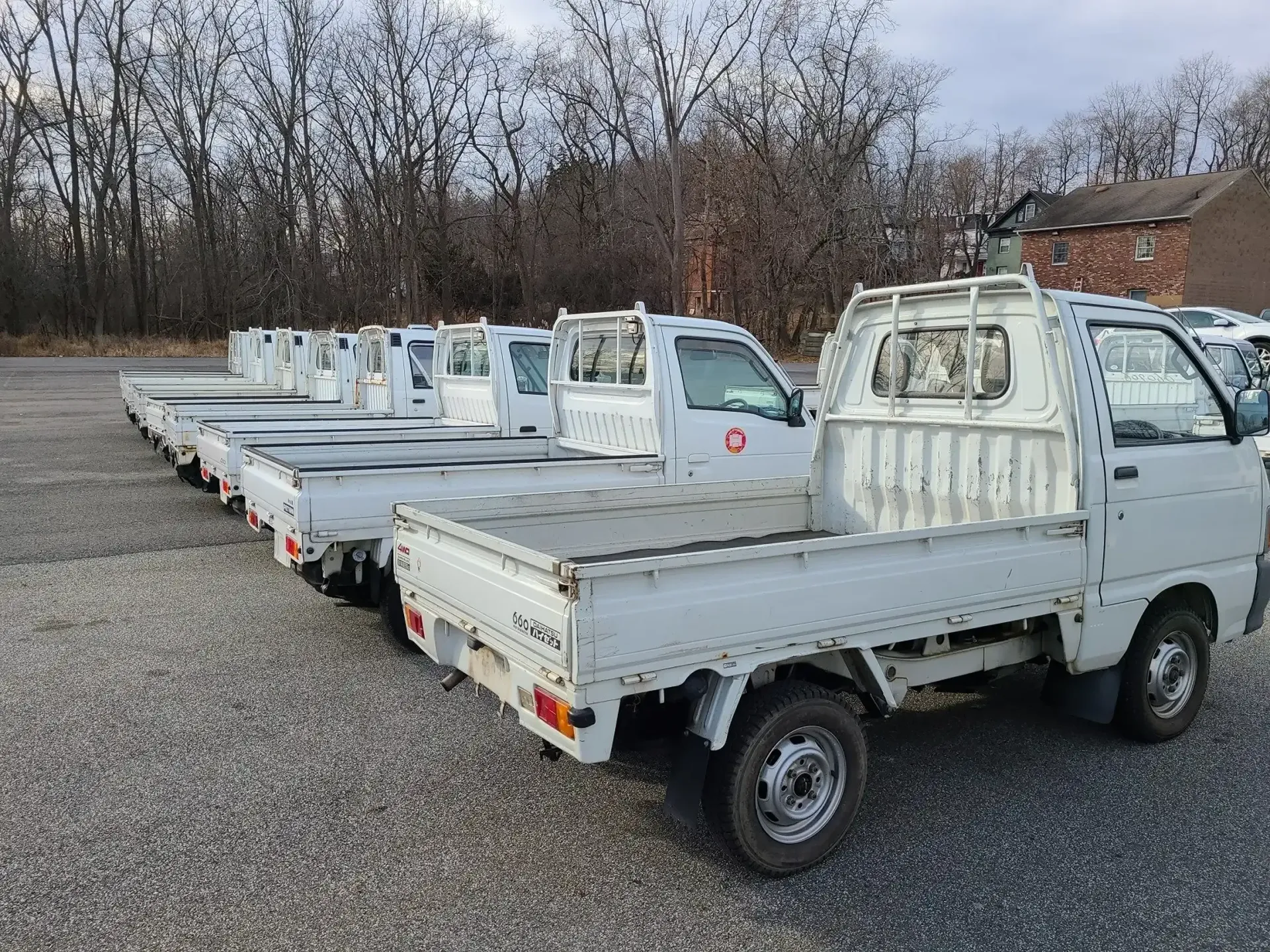 A row of white, small utility trucks parked on a gravel lot under a cloudy sky.