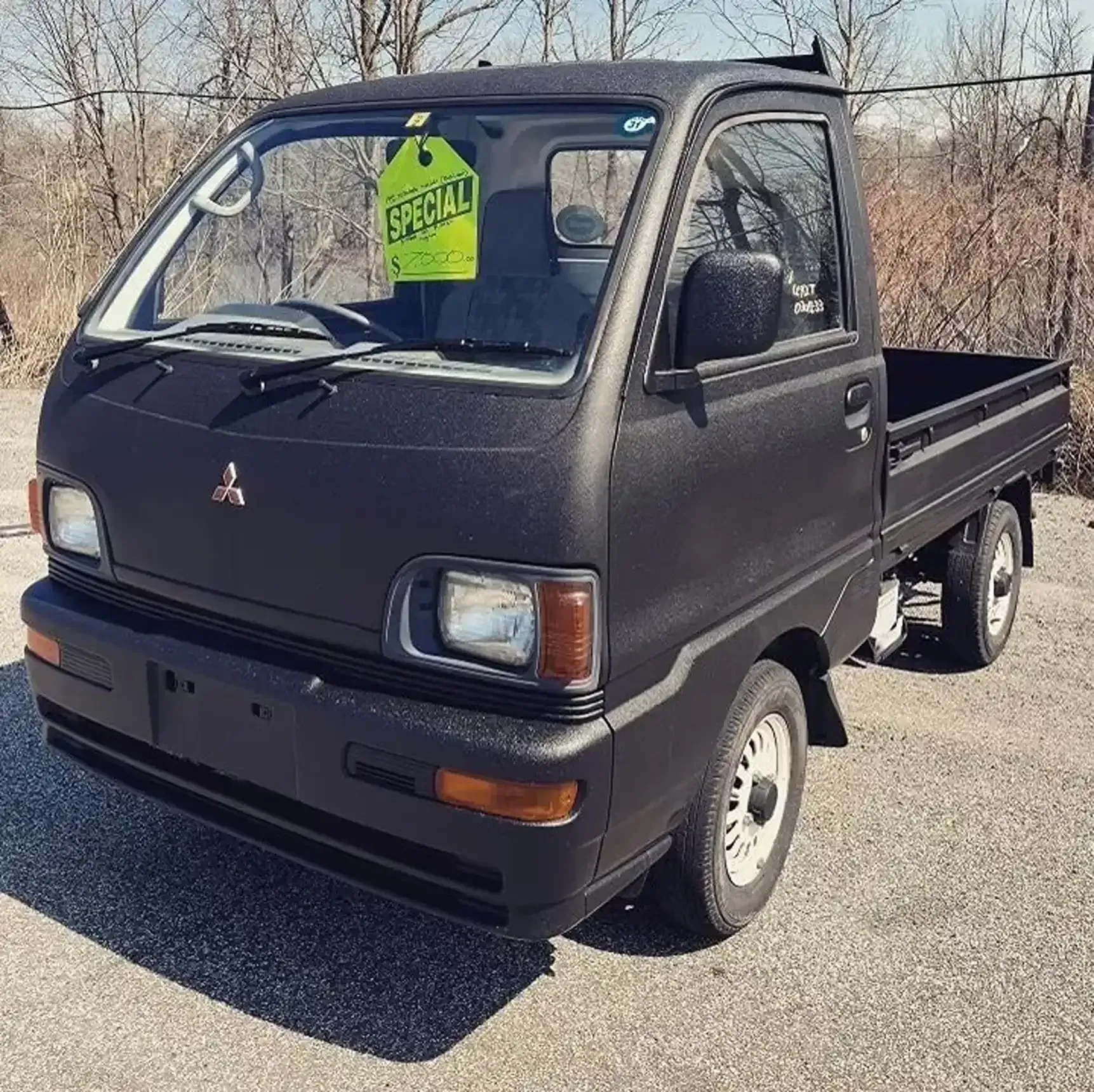 A matte black Mitsubishi kei truck parked outdoors with a yellow 