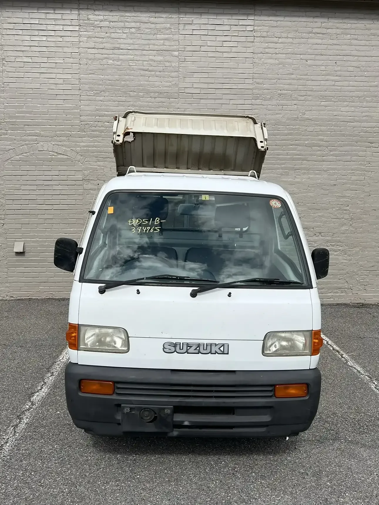 A white Suzuki kei truck parked on asphalt, featuring a black bumper and a metal rack mounted on its roof.
