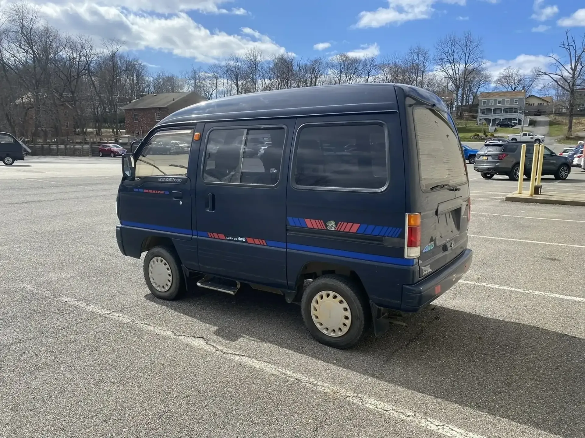 A dark blue, compact, older-model Japanese mini van parked in a gravel lot on a sunny day.