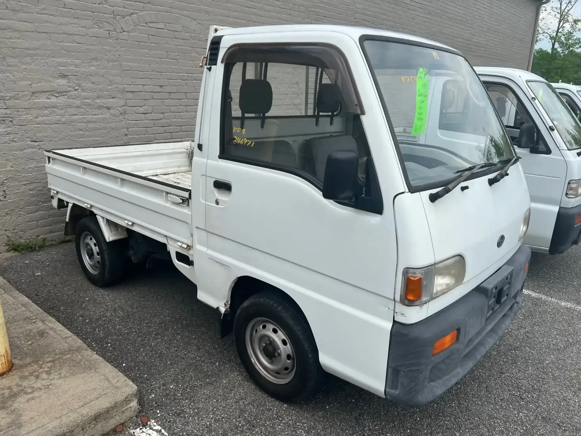 A white Japanese-style micro truck parked on an asphalt lot beside another similar vehicle.