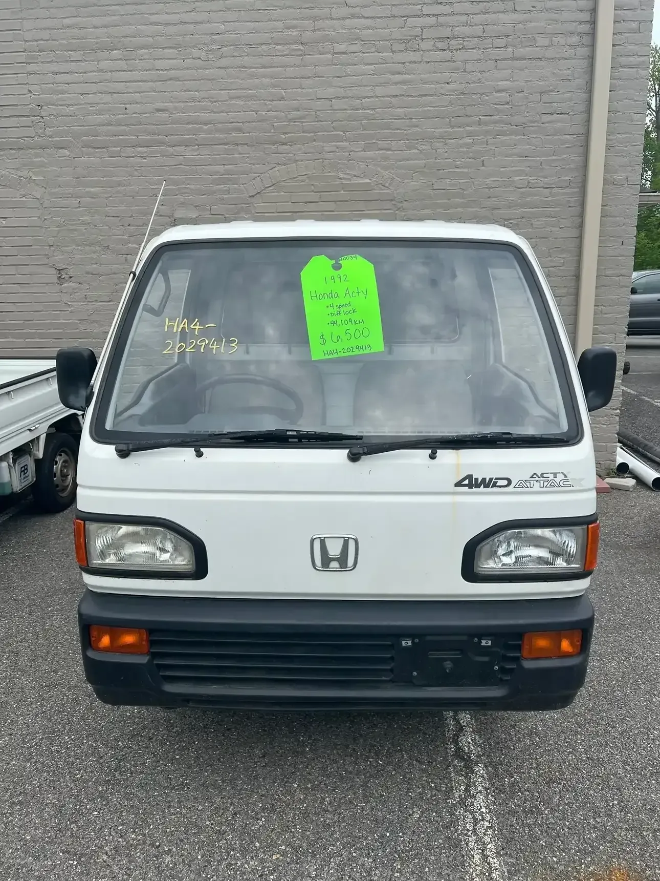 Front view of a white Honda Acty 4WD kei truck parked outdoors with a neon green sales tag in the windshield.