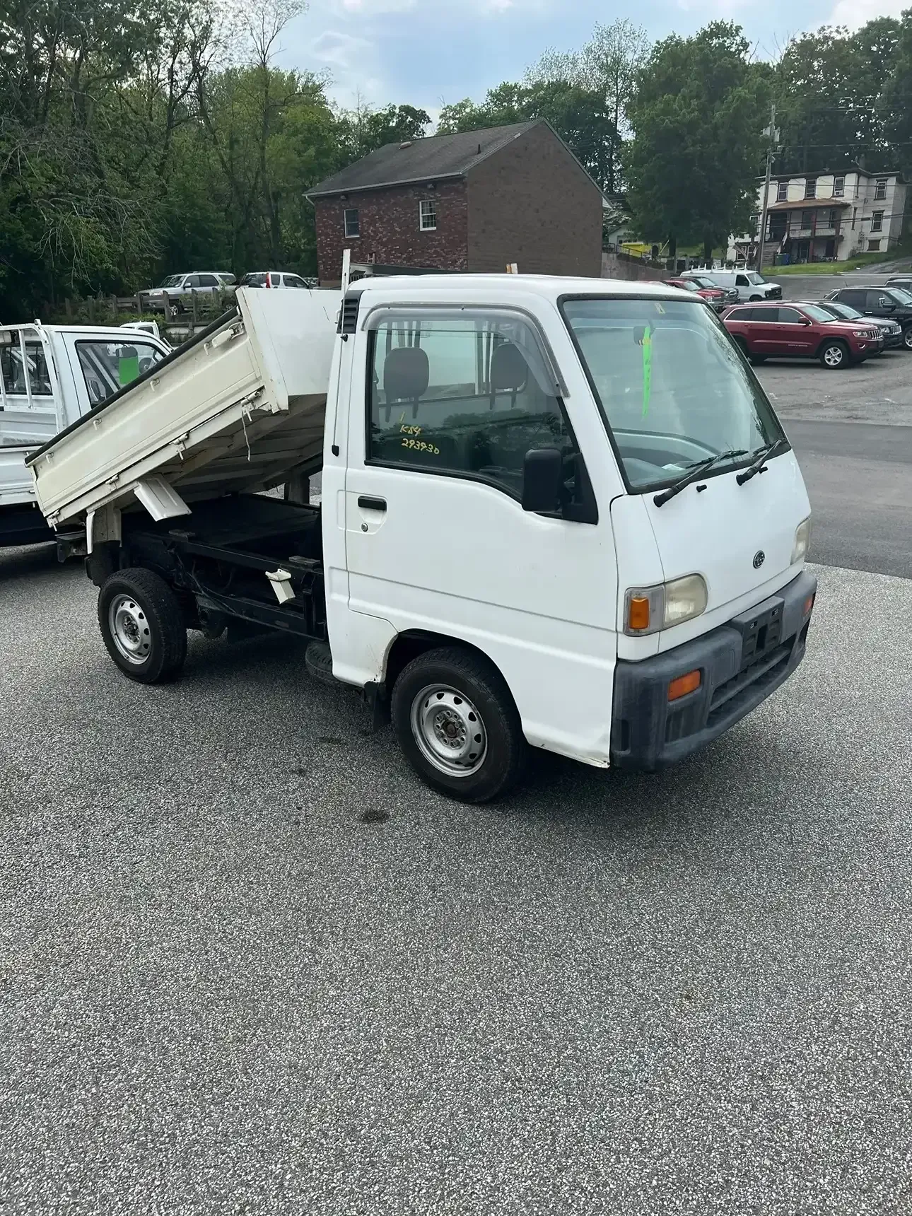 A white, compact kei dump truck parked on a gravel lot with its cargo bed partially raised.