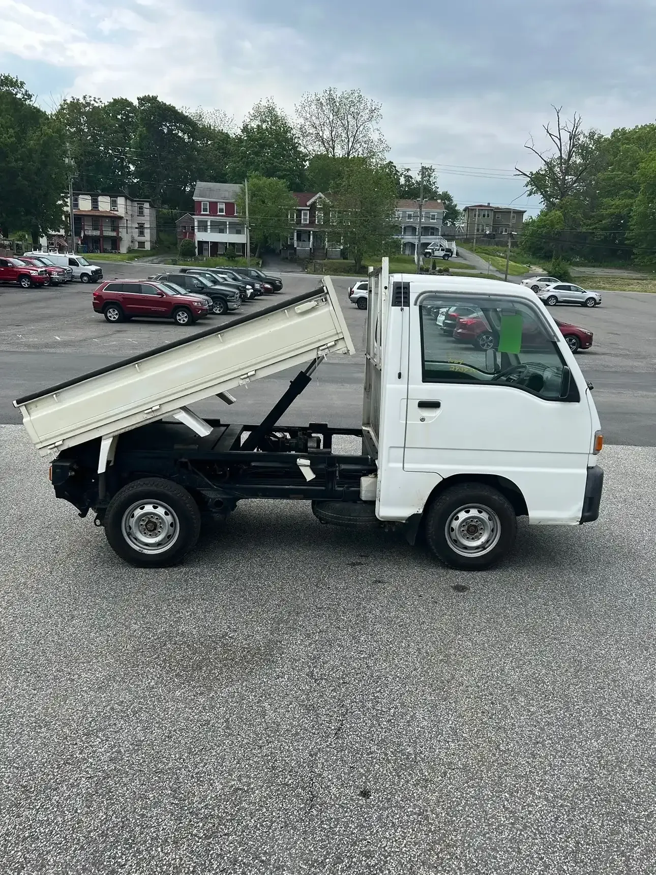 A white, small dump truck parked on a gravel lot with its cargo bed partially raised.