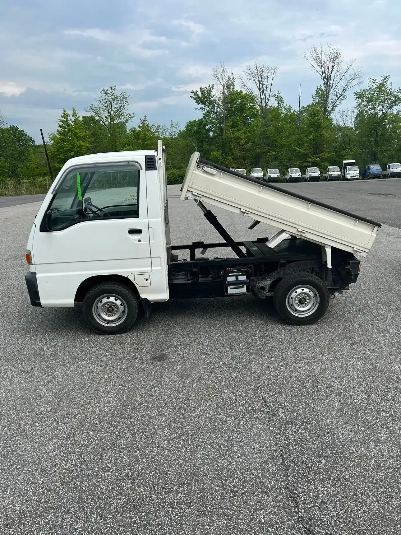 A white mini dump truck parked on a gravel lot with its bed raised in the air.