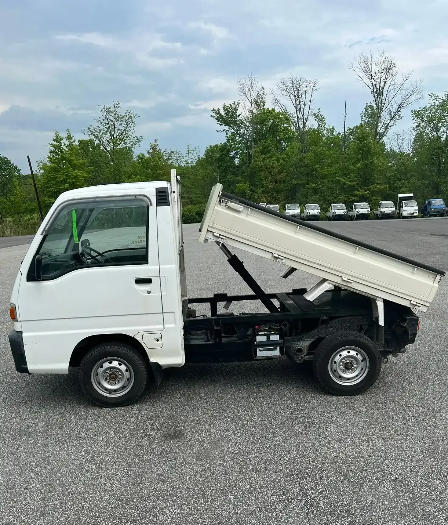 A white dump truck is parked on gravel with its bed in a raised position, with other vehicles visible in the background.
