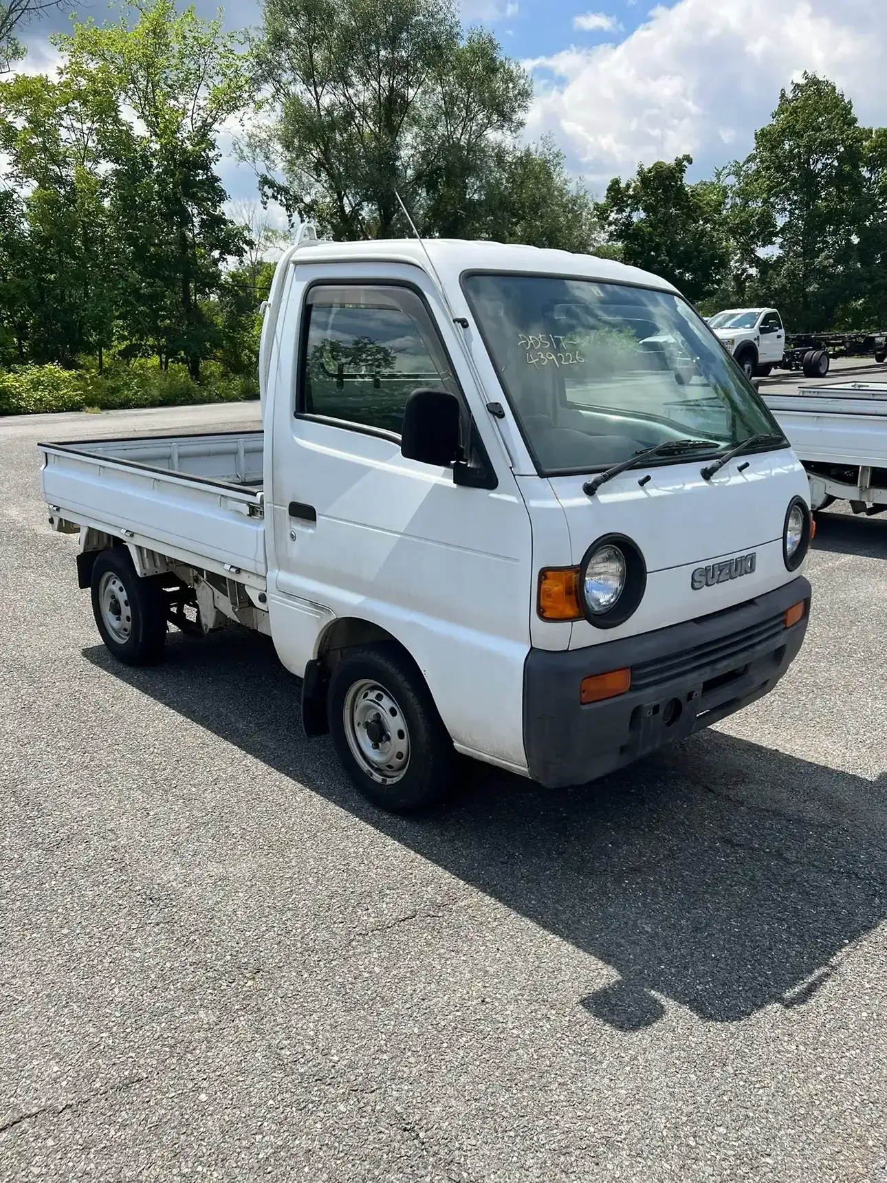 A white Mazda Scrum kei truck parked on a gravel lot under a sunny sky.