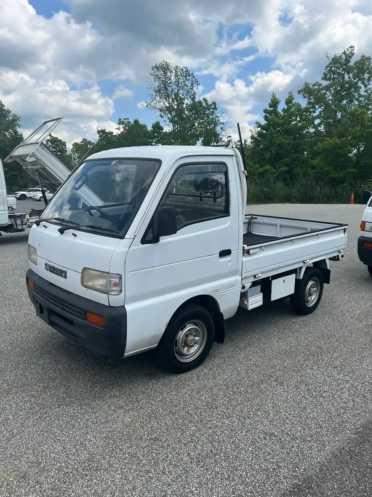 A white mini truck parked on a gravel lot under a partly cloudy sky.