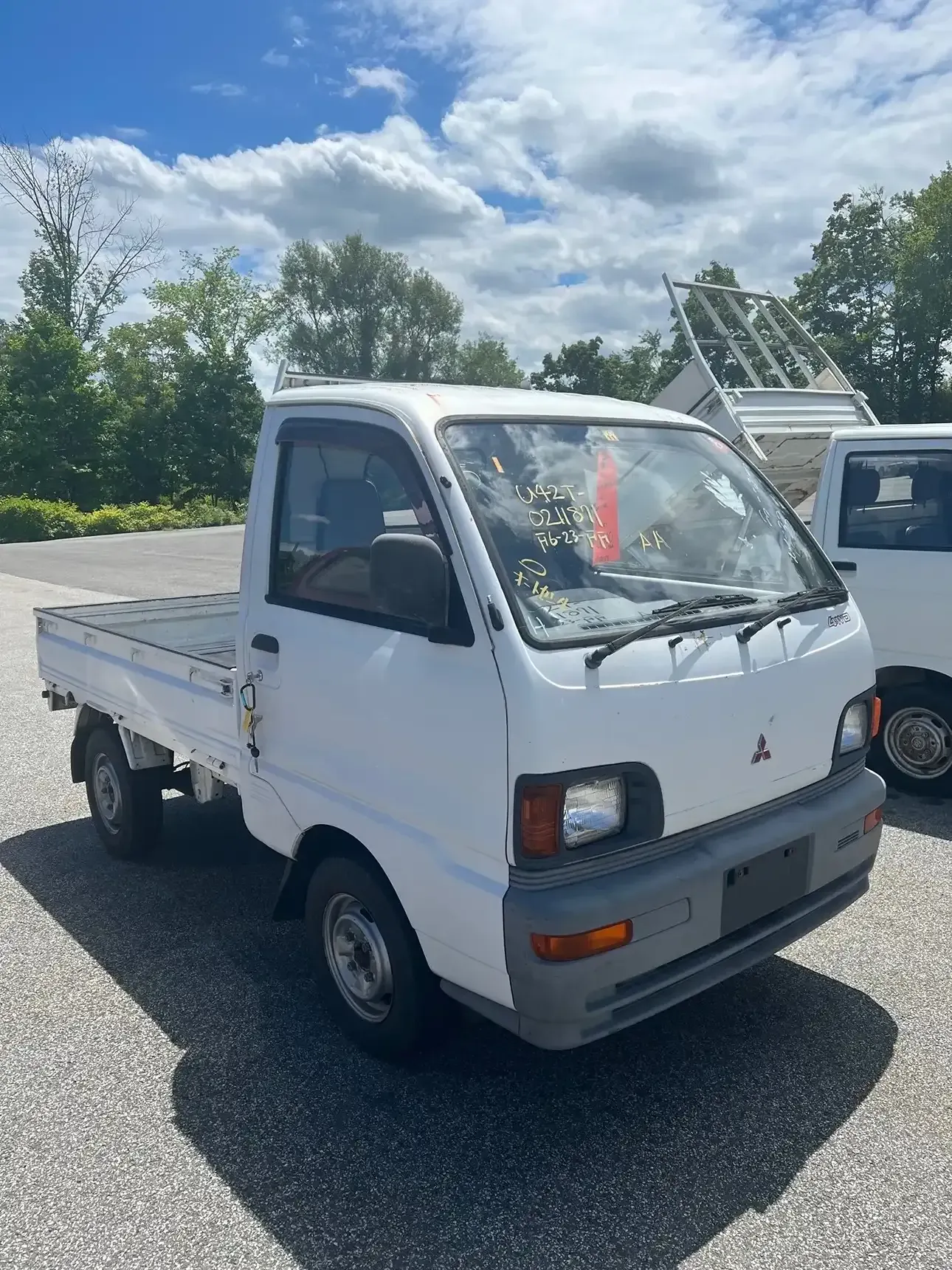 A white Mitsubishi kei truck parked outdoors on a sunny day with a partly cloudy sky.