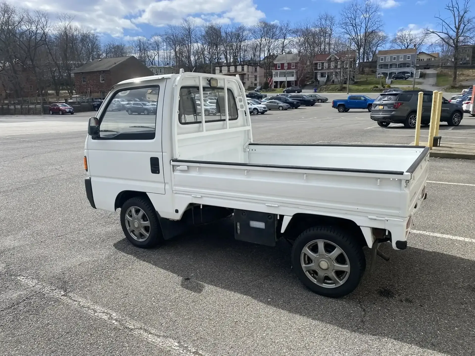 A white, Japanese-style compact kei truck parked in a large, paved parking lot on a sunny day.