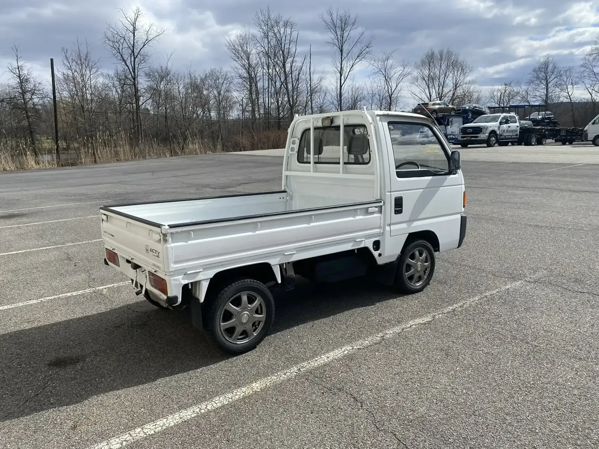 A white Kei truck parked in a gravel lot under a cloudy sky.