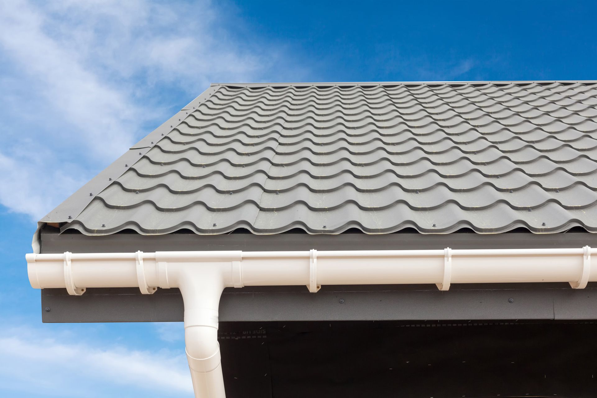A close up of a roof with a white gutter and a blue sky in the background.