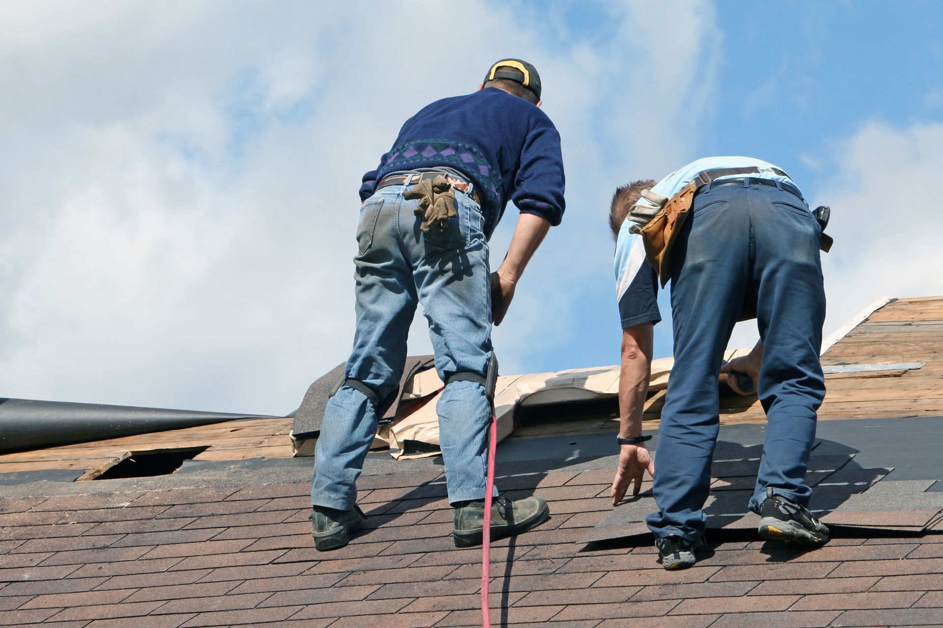 Two workers are repairing roof shingles on a house
