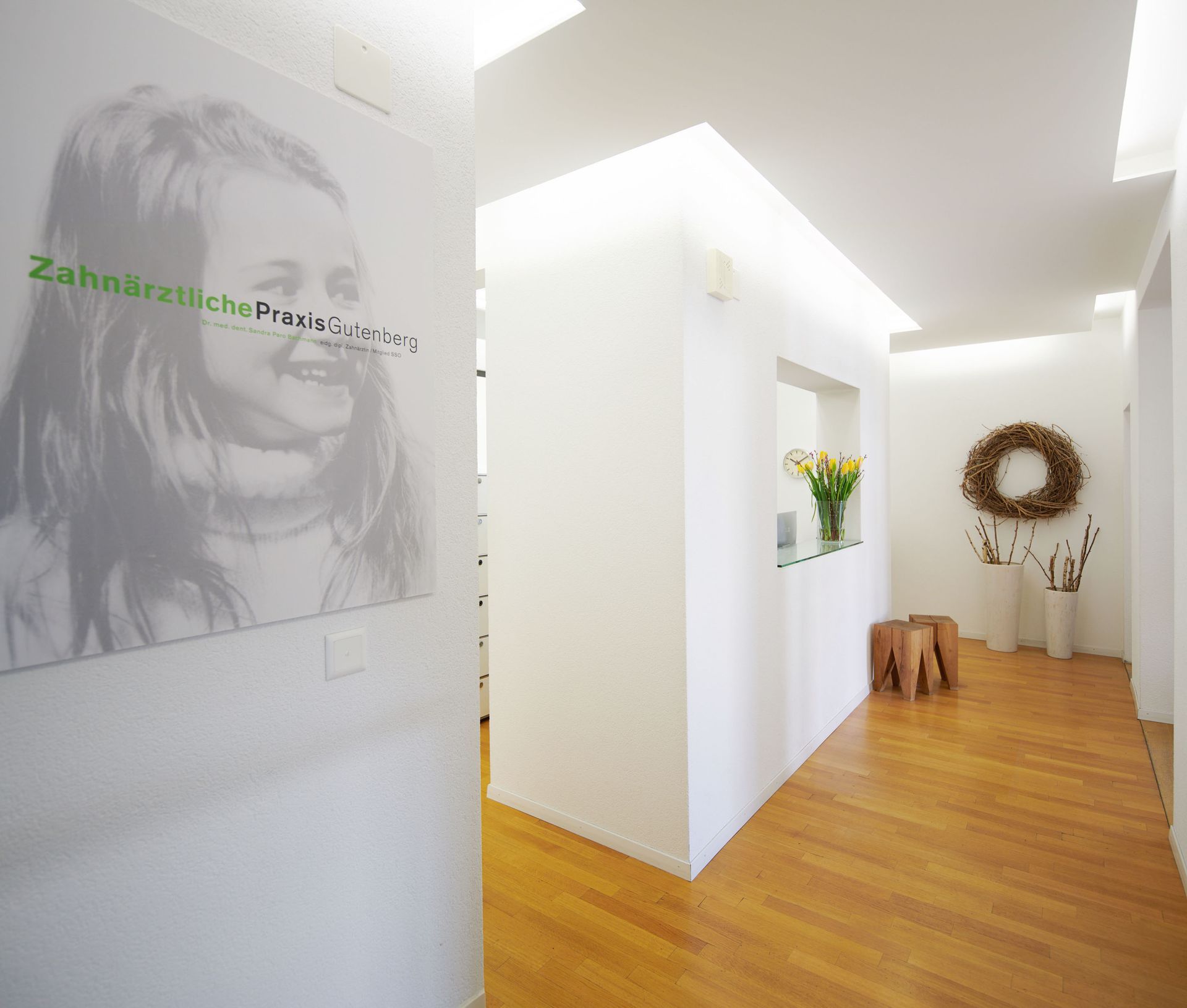 Modernes Interieur einer Zahnarztpraxis mit einem grossen Porträt an der Wand, Holzböden und einem weissen Empfangstresen.