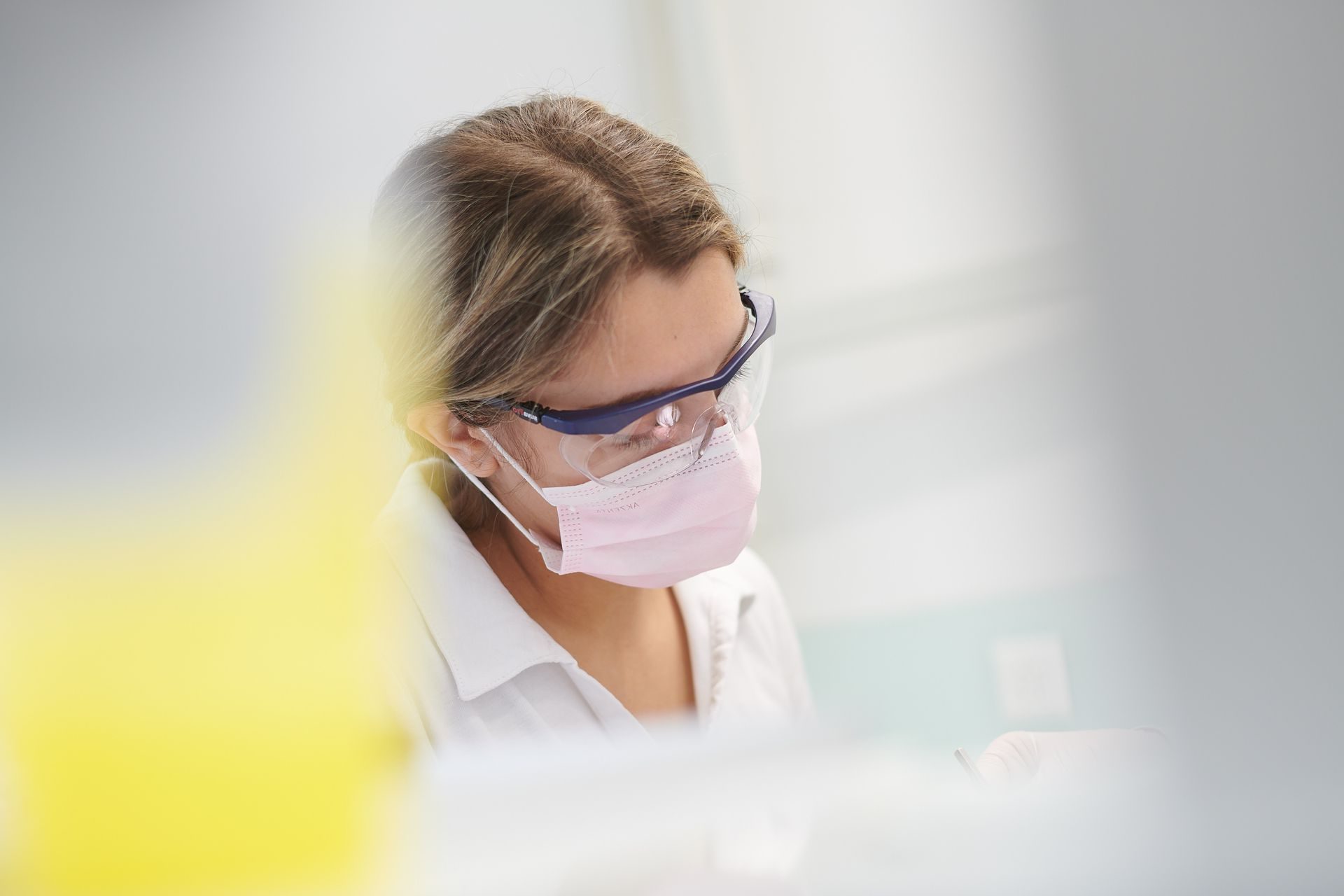 Eine Dentalassistentin in weissem Hemd, Brille und Mundschutz, die in einer zahnärztlichen Einrichtung arbeitet.