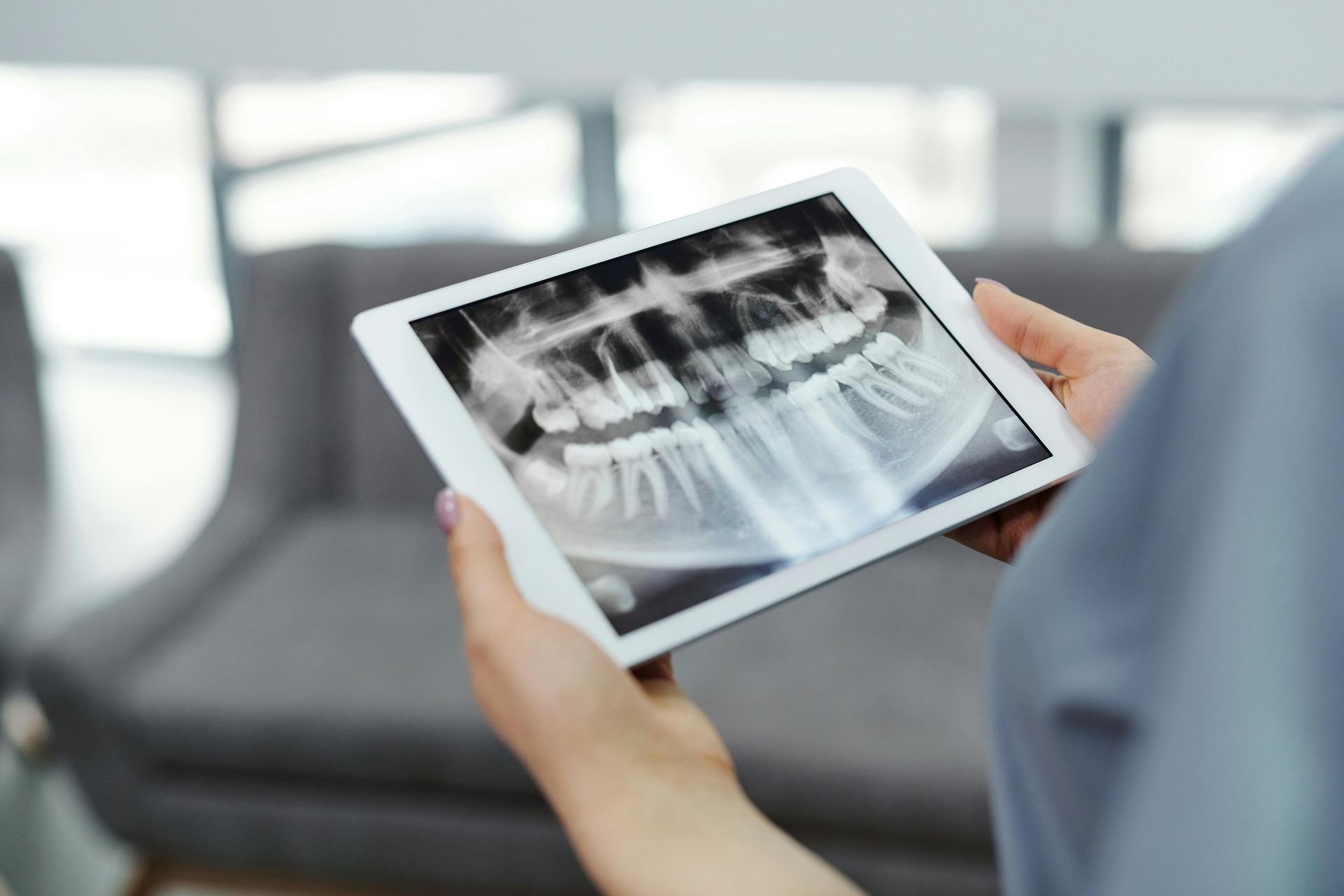 Hände halten ein Tablet, auf dem ein zahnärztliches Röntgenbild angezeigt wird, in einer Klinikumgebung