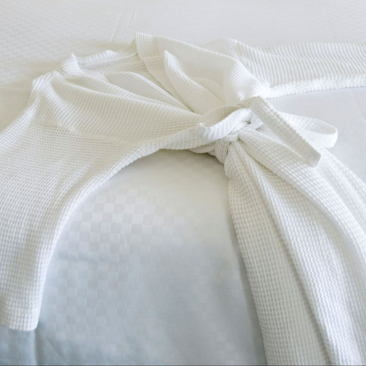 A white robe is sitting on top of a white bed.