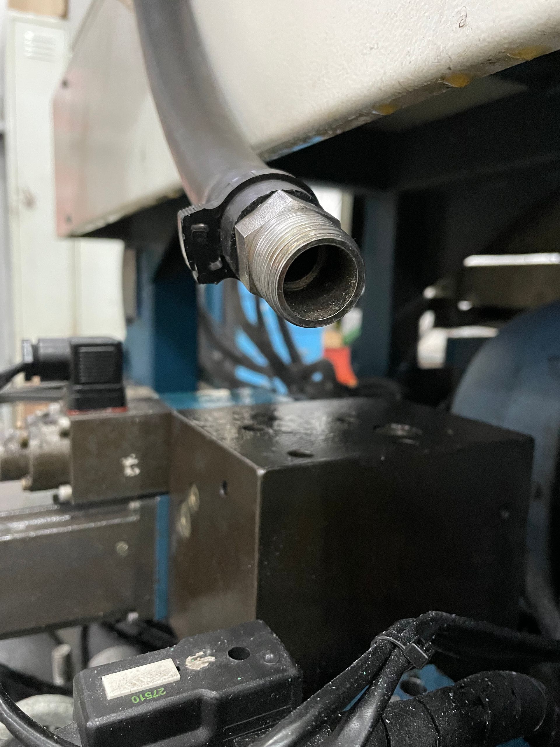 Un primer plano de una boquilla de una máquina conectada a una manguera gris, con gotas de agua en la superficie debajo.