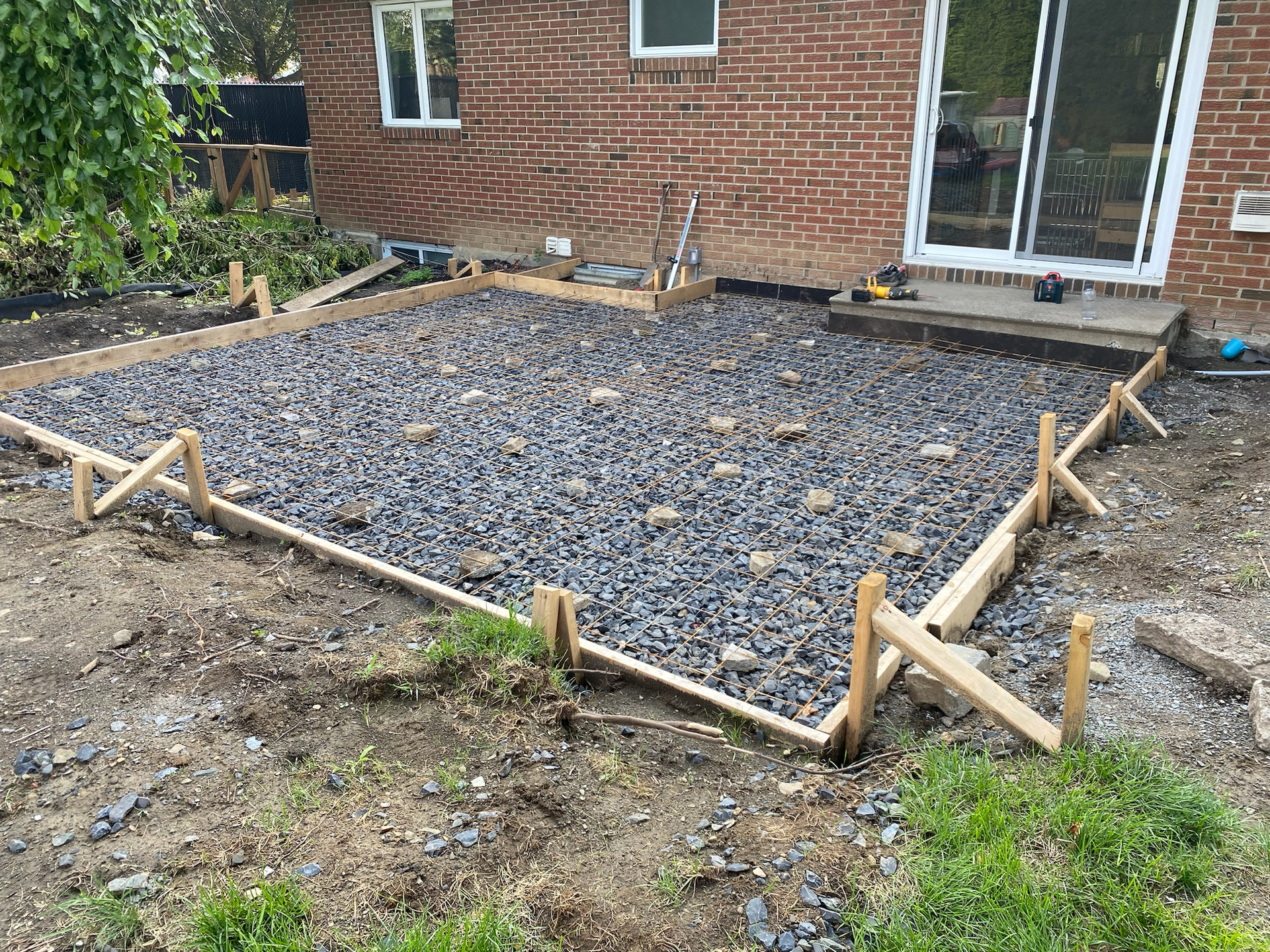 A patio is being built in the backyard of a brick house.