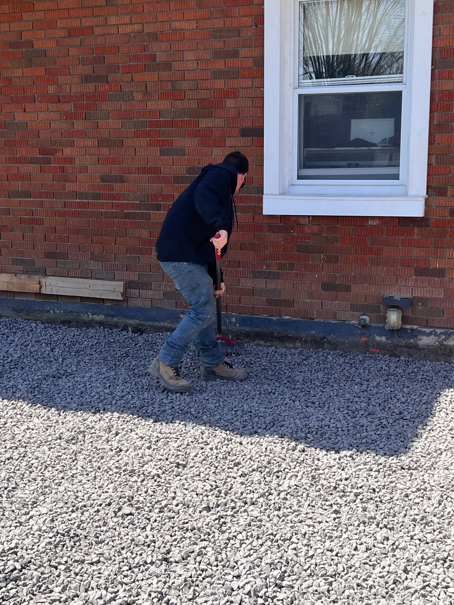 A man is standing in front of a brick building holding a shovel.