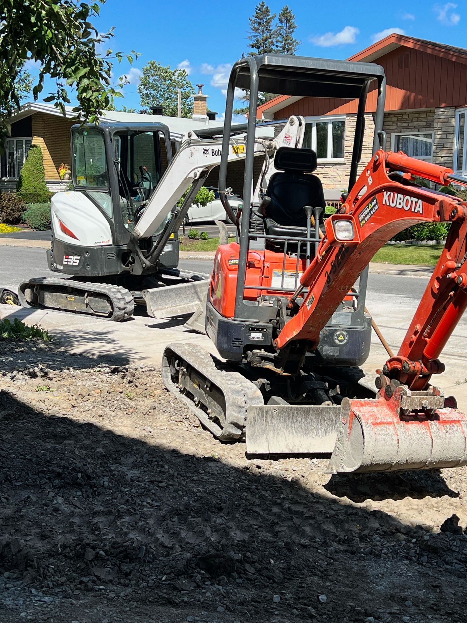 Two excavators are working on a construction site in front of a house.