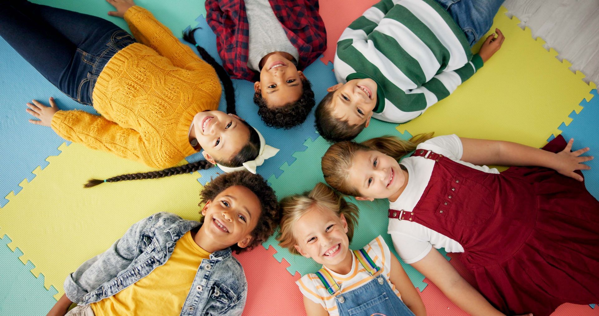 Children smiling in a circle on a classroom mat during a fun preschool bonding and learning activity