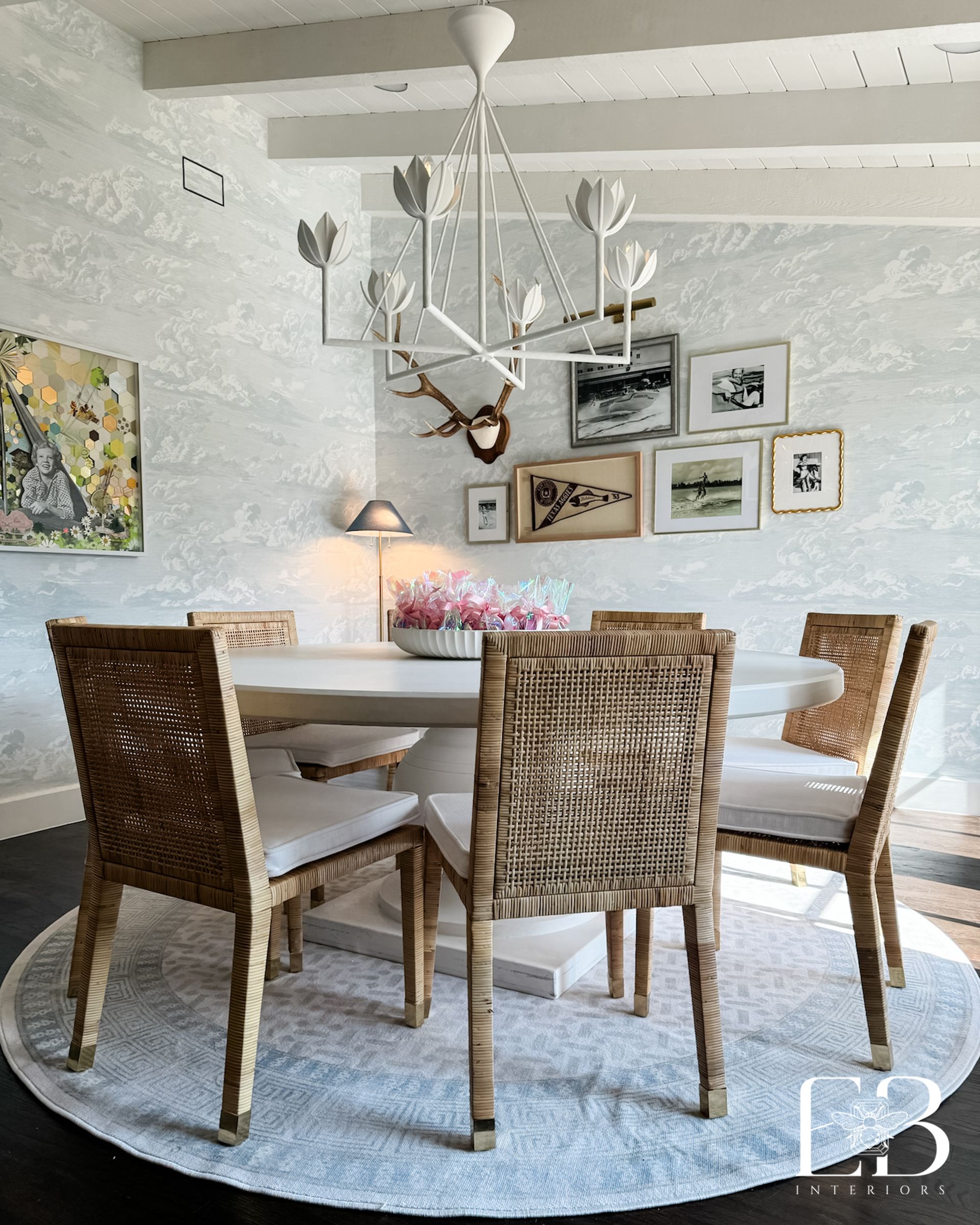 Transitional dining room by Emerald Bee Interiors with rattan chairs, white chandelier, and cloud-pattern wallpaper.