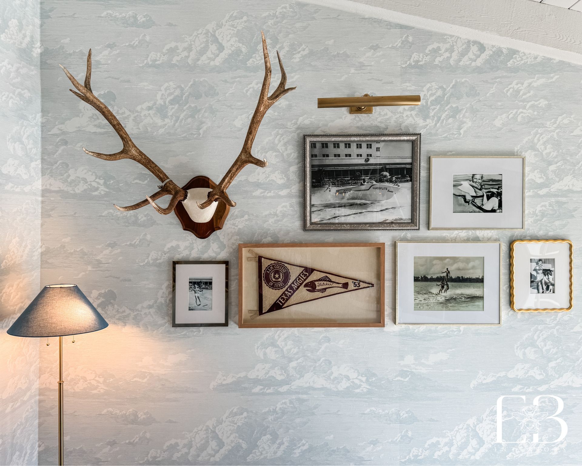 Vintage gallery wall with antler mount and black-and-white photos on cloud wallpaper by Emerald Bee Interiors.