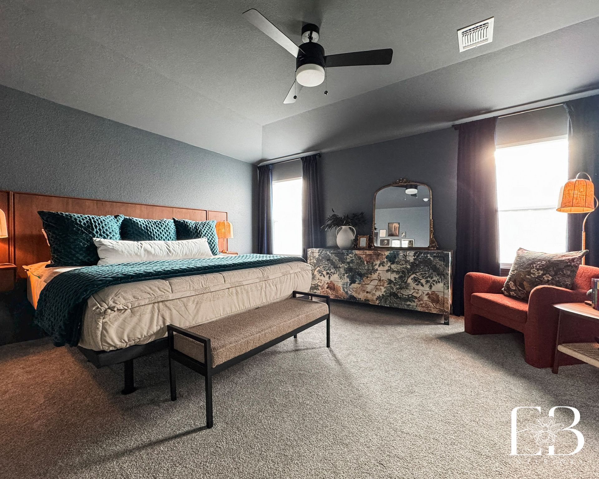 Moody modern bedroom by Emerald Bee Interiors with blue-gray walls, teal bedding, and a botanical mural dresser.