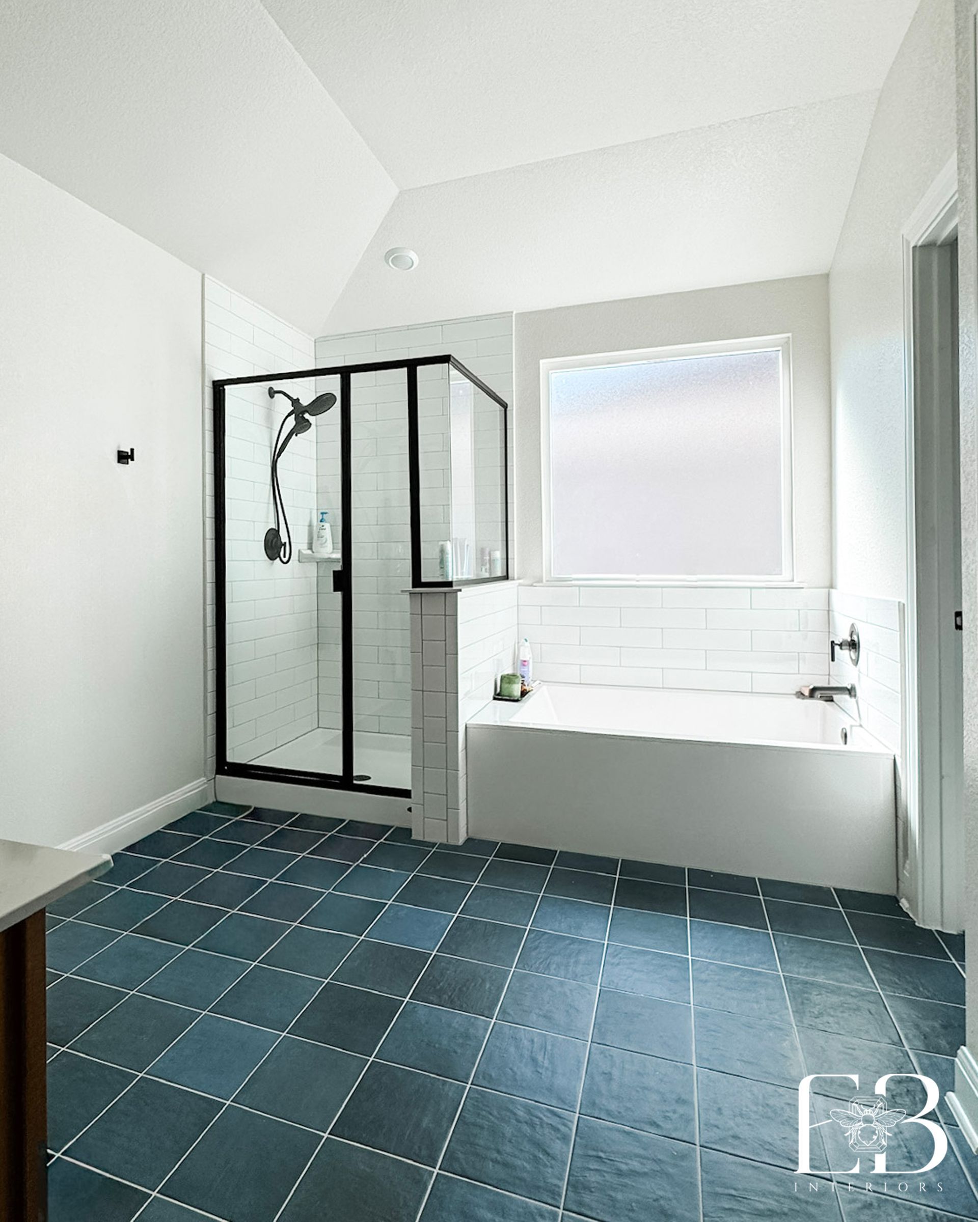 Primary bathroom by Emerald Bee Interiors with slate-blue floors, white subway tile, and black-framed shower enclosure.