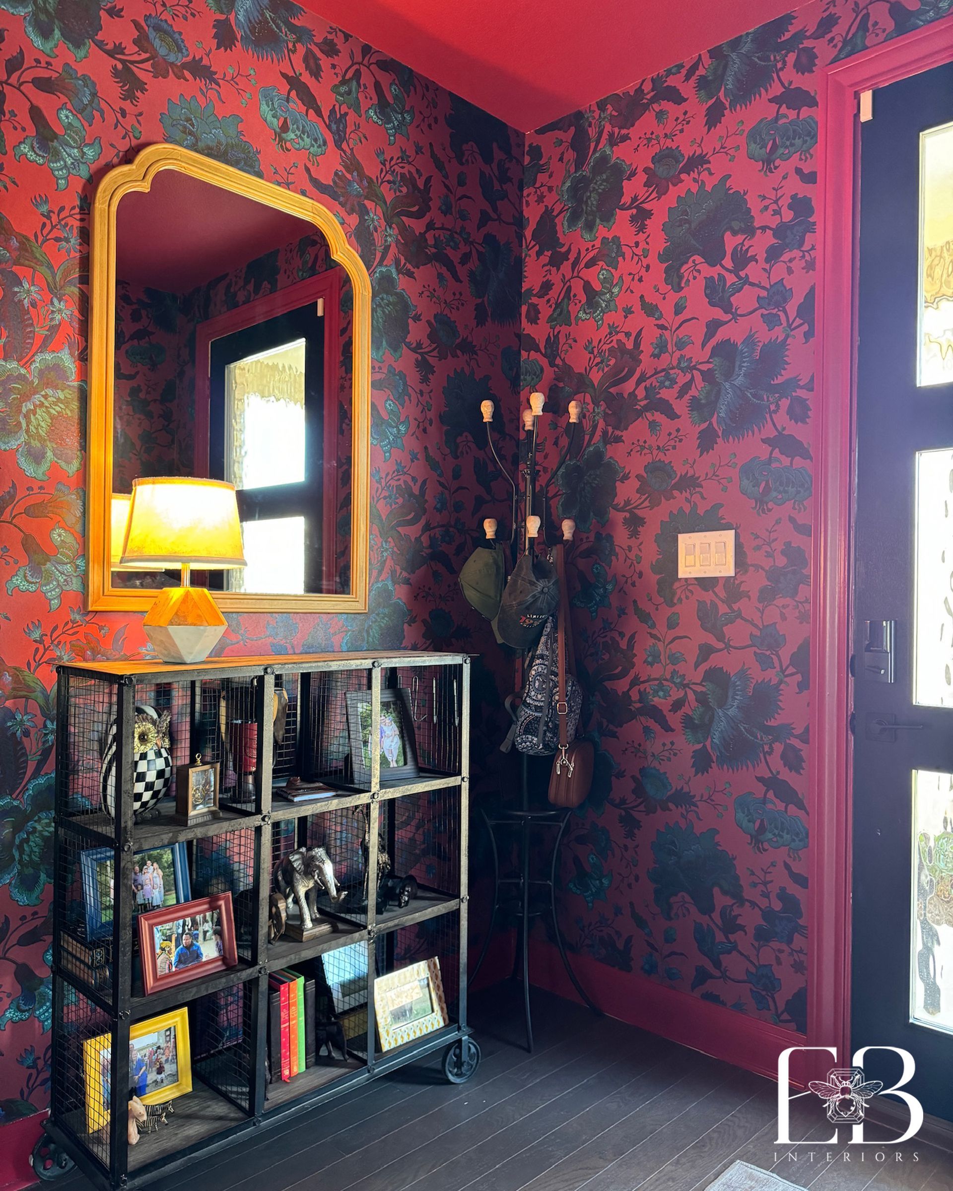 Red entryway by Emerald Bee Interiors with floral wallpaper, vintage mirror, and industrial shelving for a dramatic look.