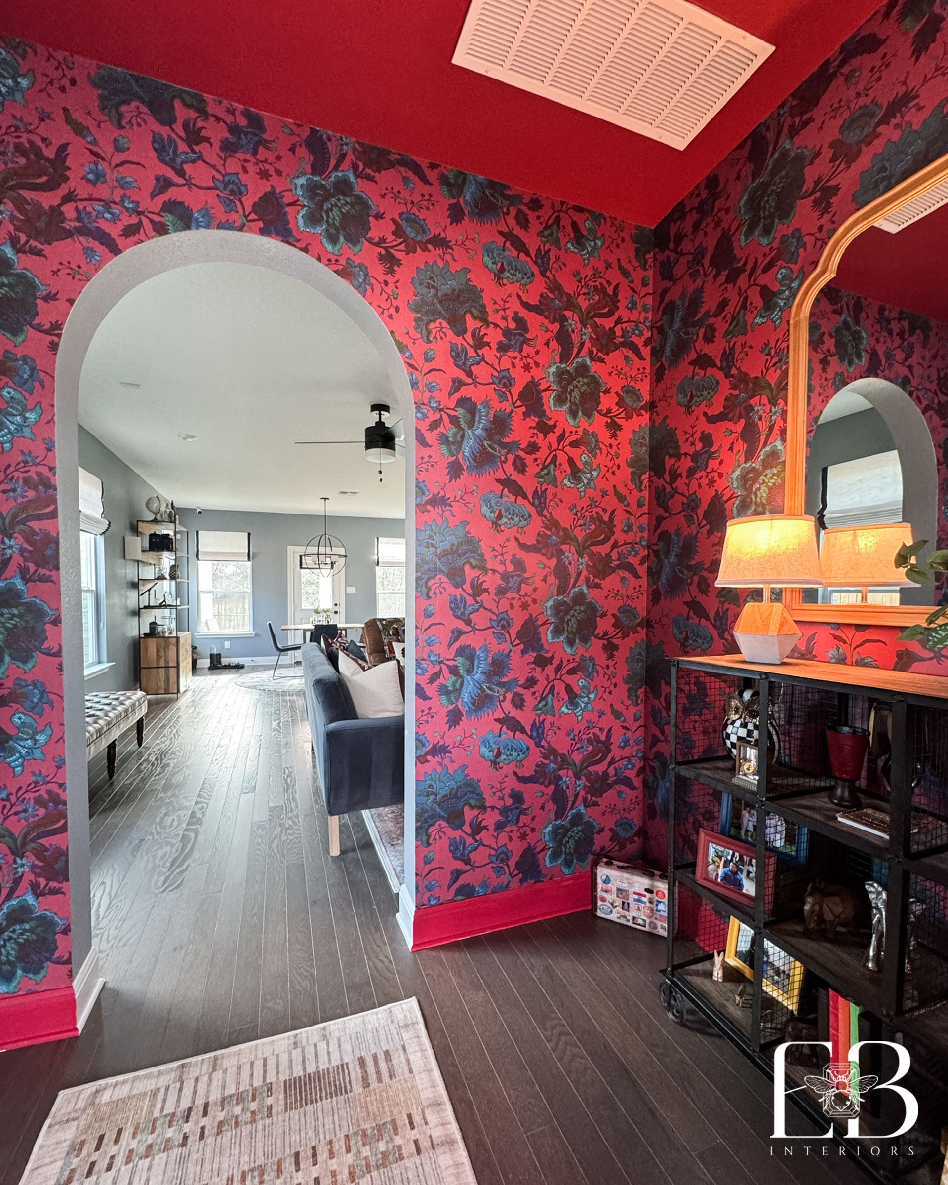 Red entryway by Emerald Bee Interiors featuring floral wallpaper, vintage mirror, and industrial shelving for dramatic look.