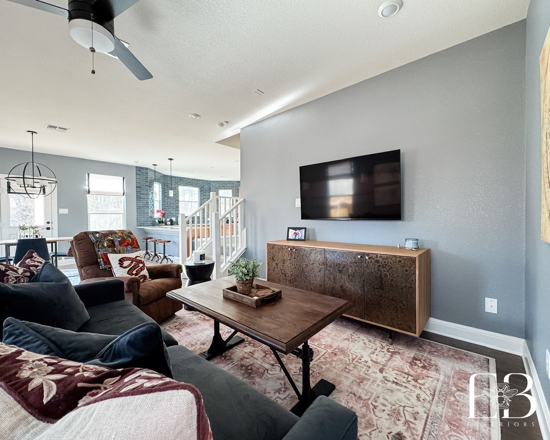 Open living room with soft blue walls, wood media console, and leather recliner by Emerald Bee Interiors for warm contrast.