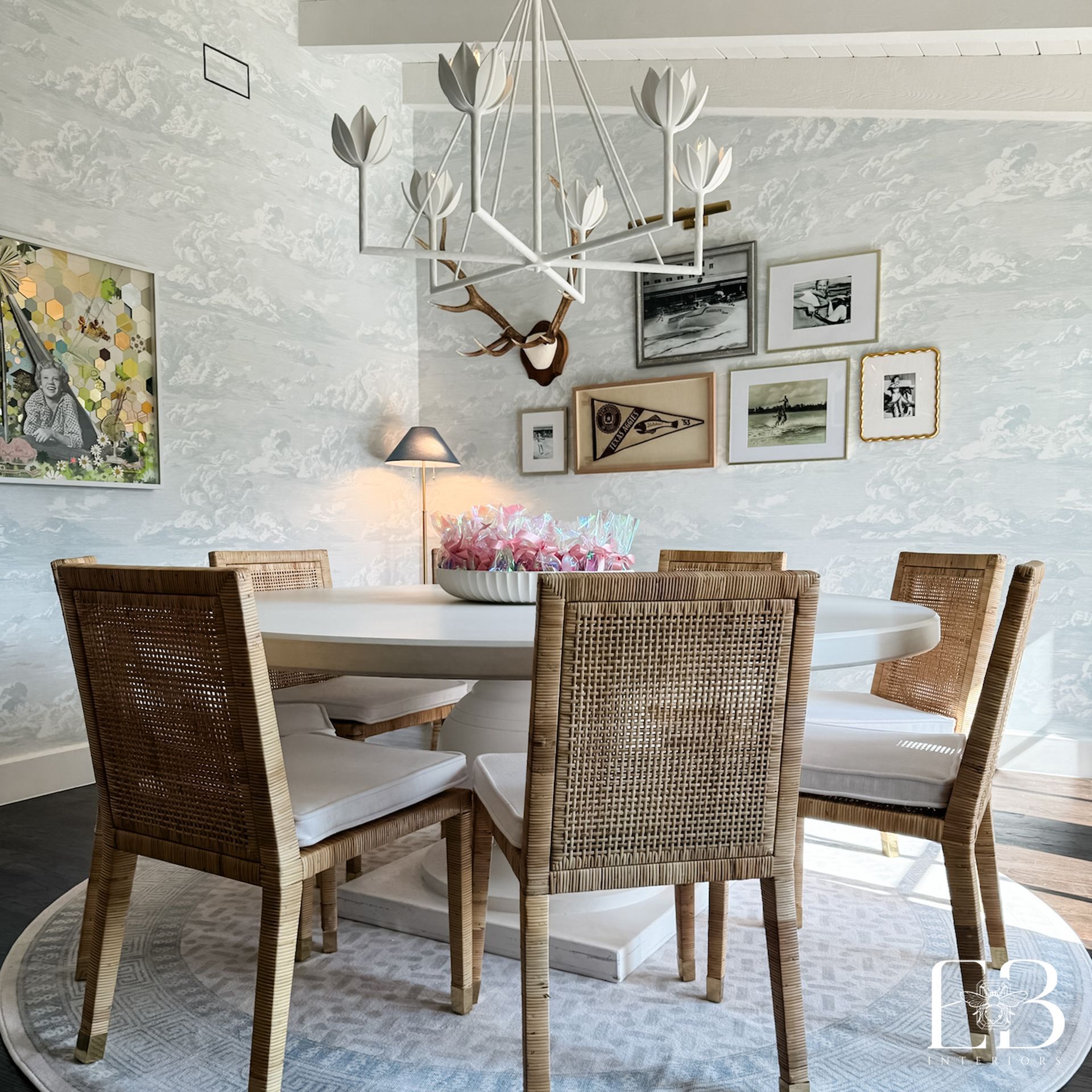 Dining room with round table, woven chairs, art, and a decorative chandelier.