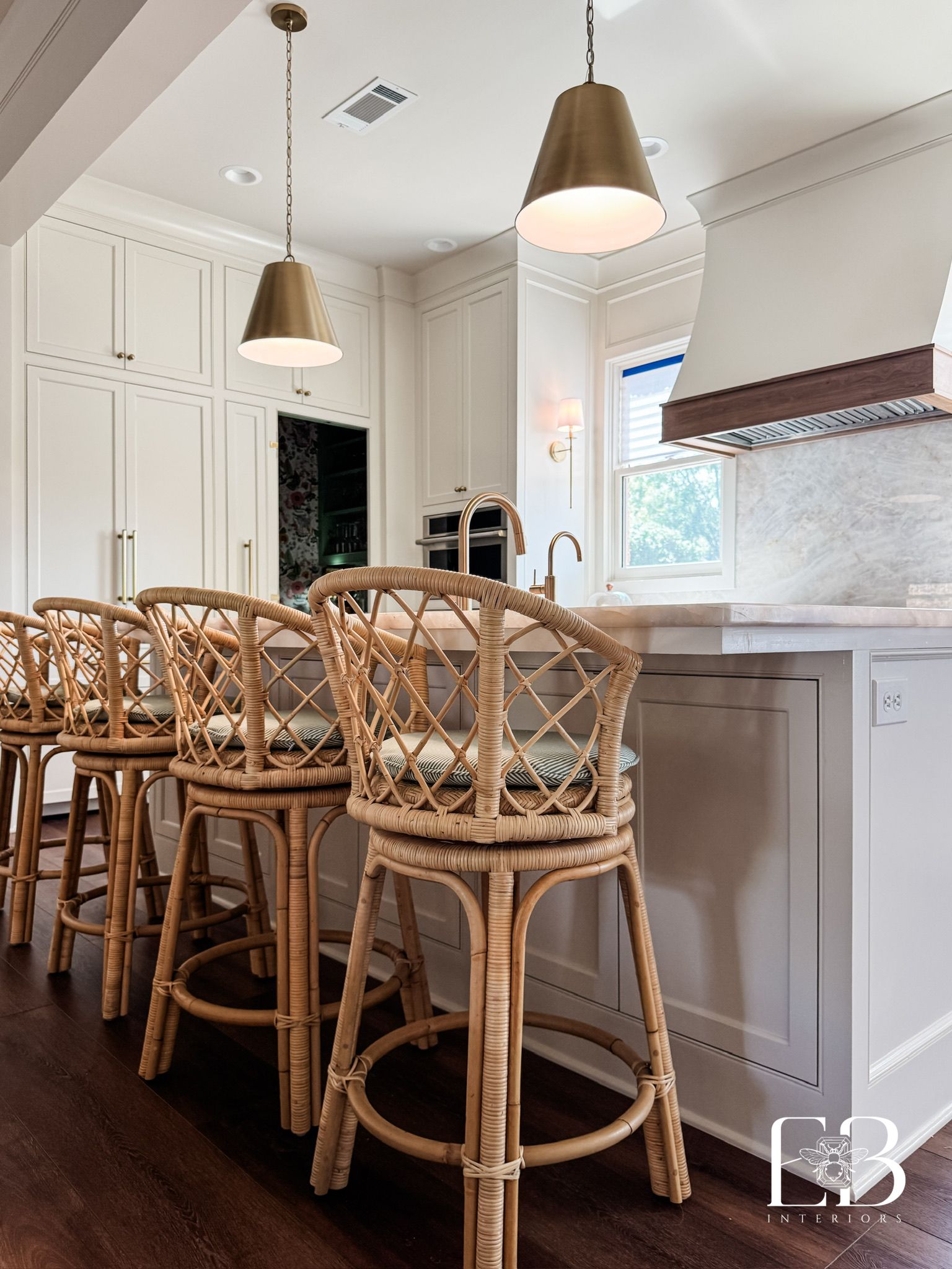 Kitchen with rattan bar stools, white cabinets, and gold pendant lights.