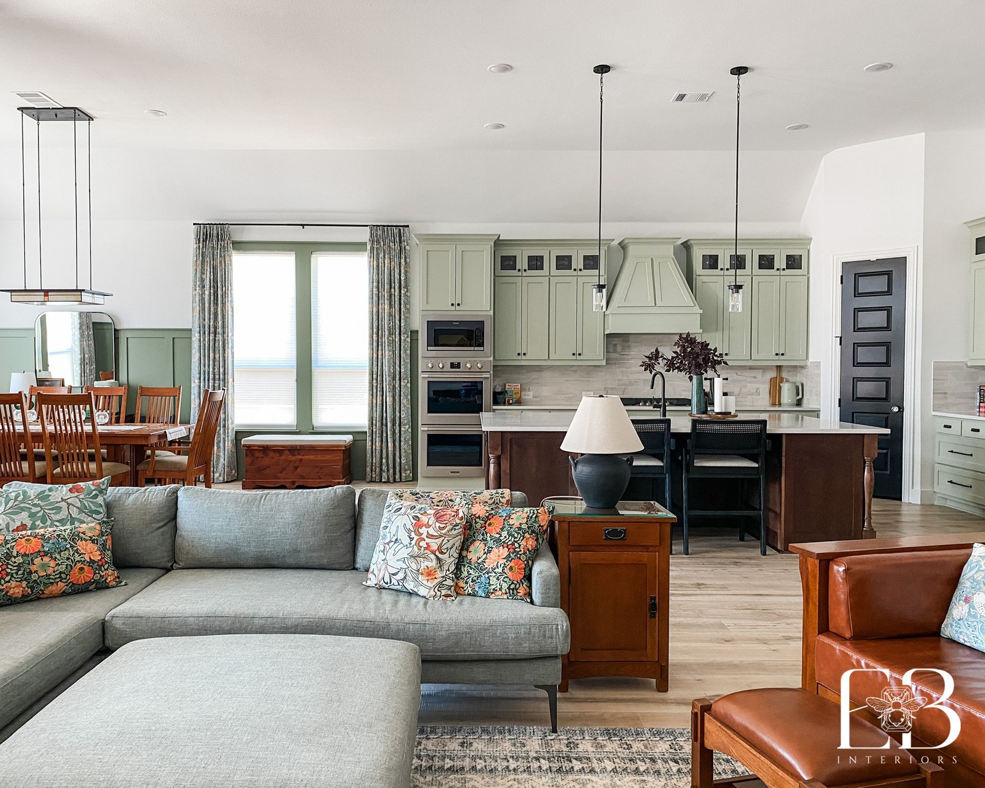 Spacious open-concept living space with gray sofa, sage green kitchen cabinets, and wooden dining set.
