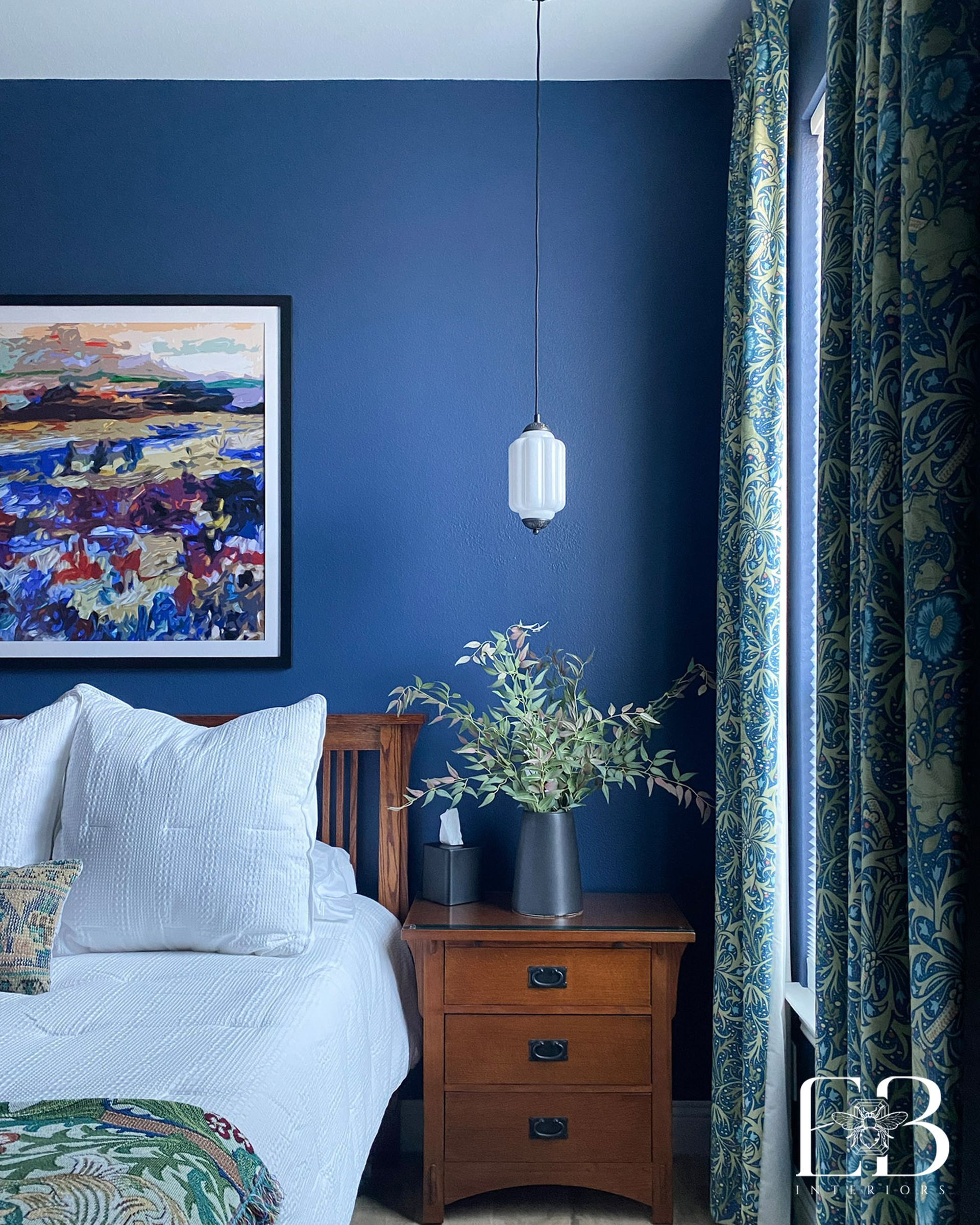 Guest room with blue patterned curtains, mission nightstand, and greenery accent designed by Emerald Bee Interiors.