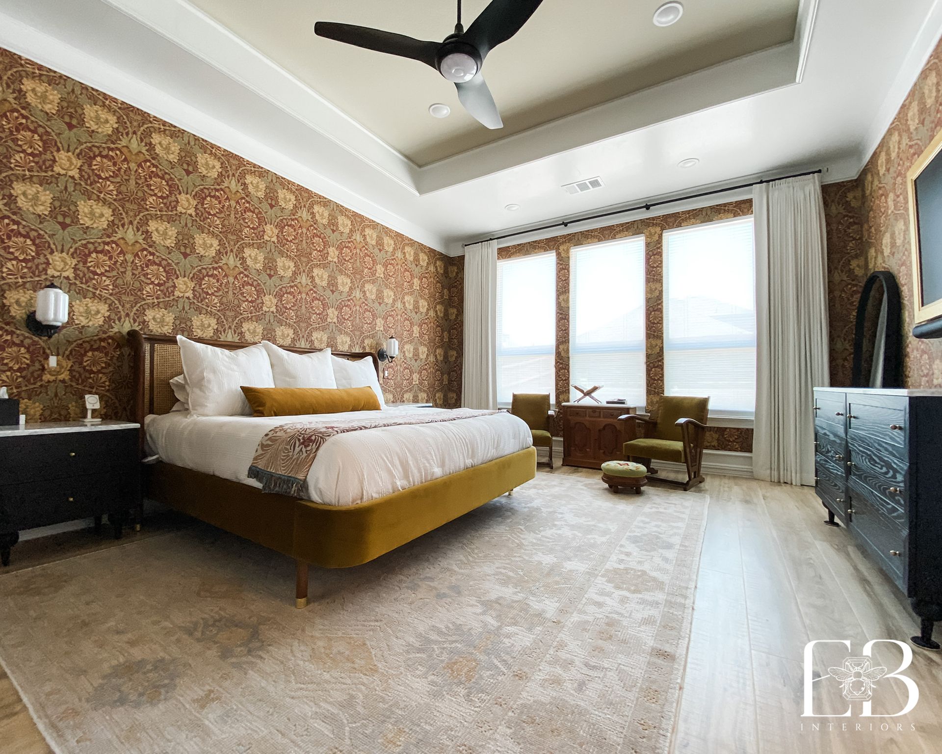 Primary bedroom by Emerald Bee Interiors with William Morris wallpaper, mustard velvet bed, and black nightstands.