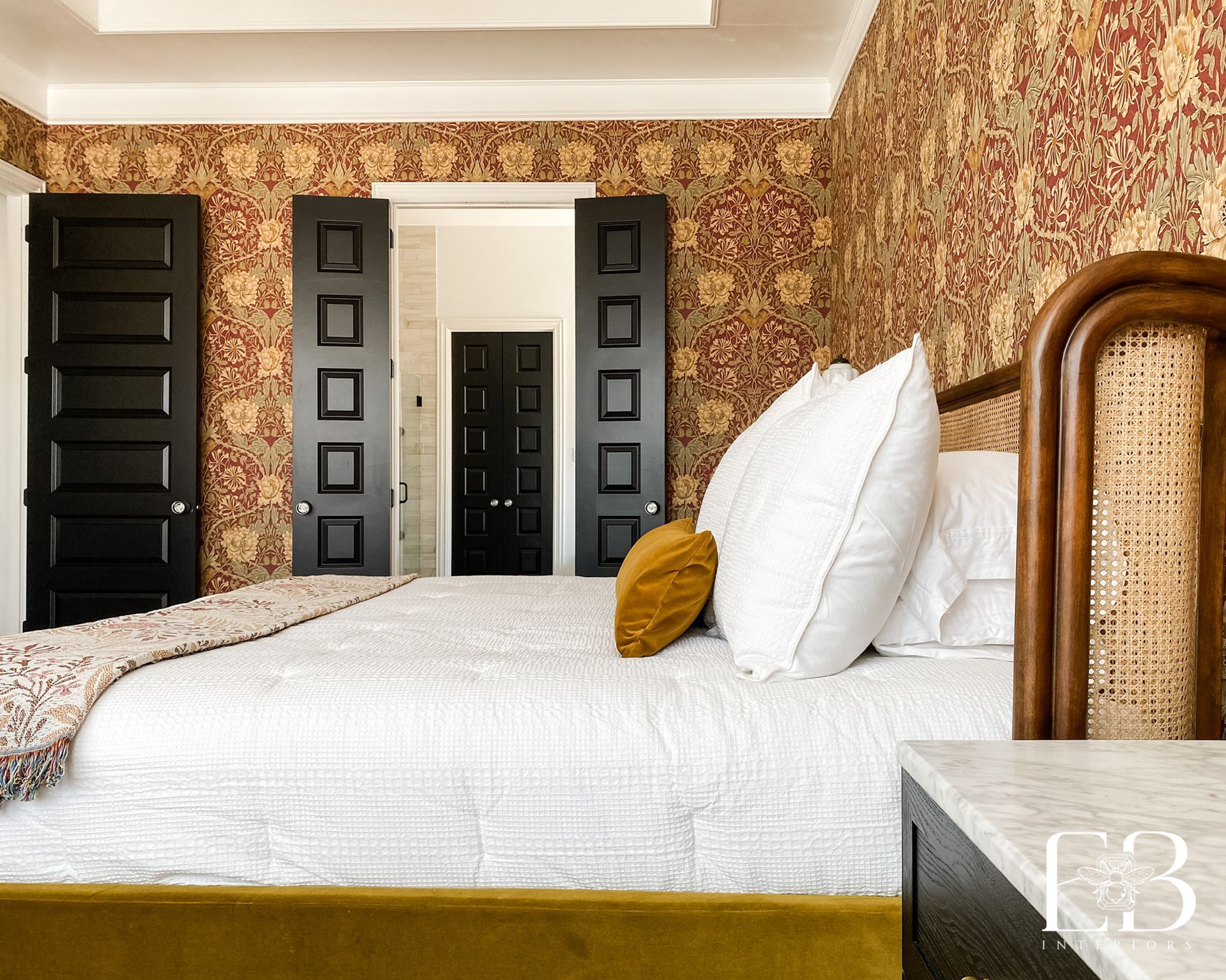 Bedroom with floral wallpaper, black doors, and a bed with white bedding and a cane headboard.