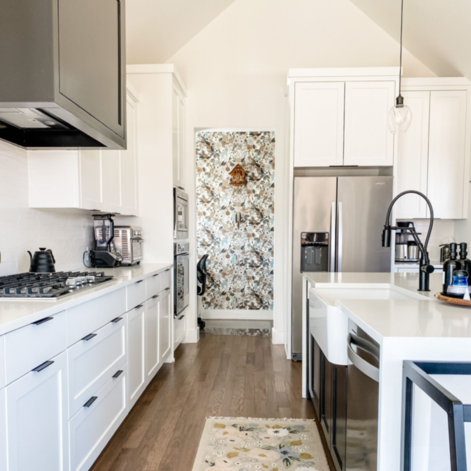 Transitional kitchen by Emerald Bee Interiors with white cabinets, oak floors, black accents, and a floral wallpaper nook.