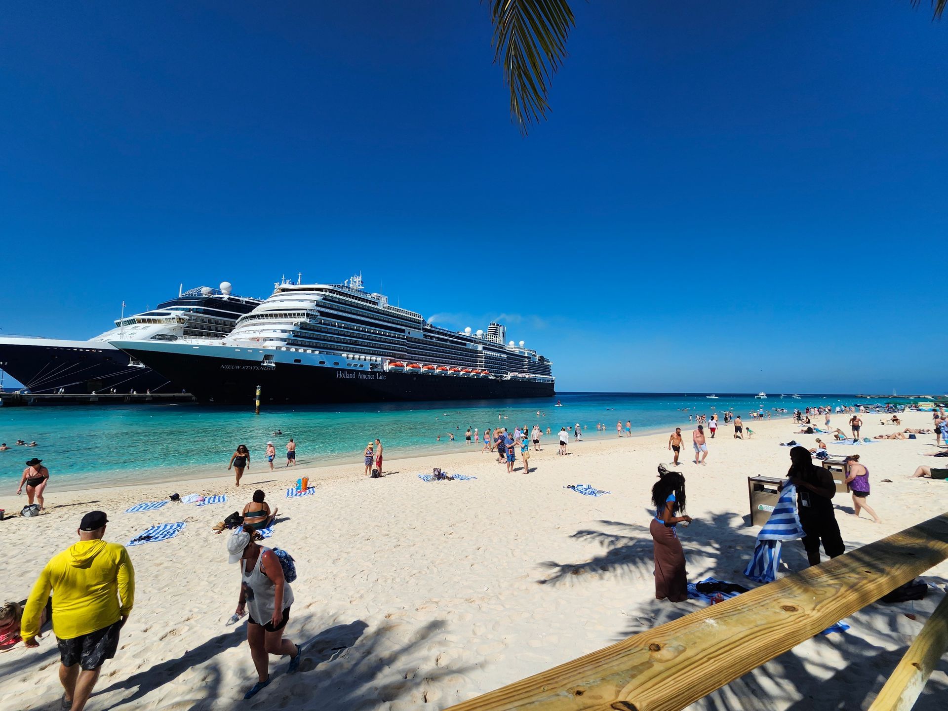 Beach scene with a large cruise ship in the background, blue sky, people on the sand.